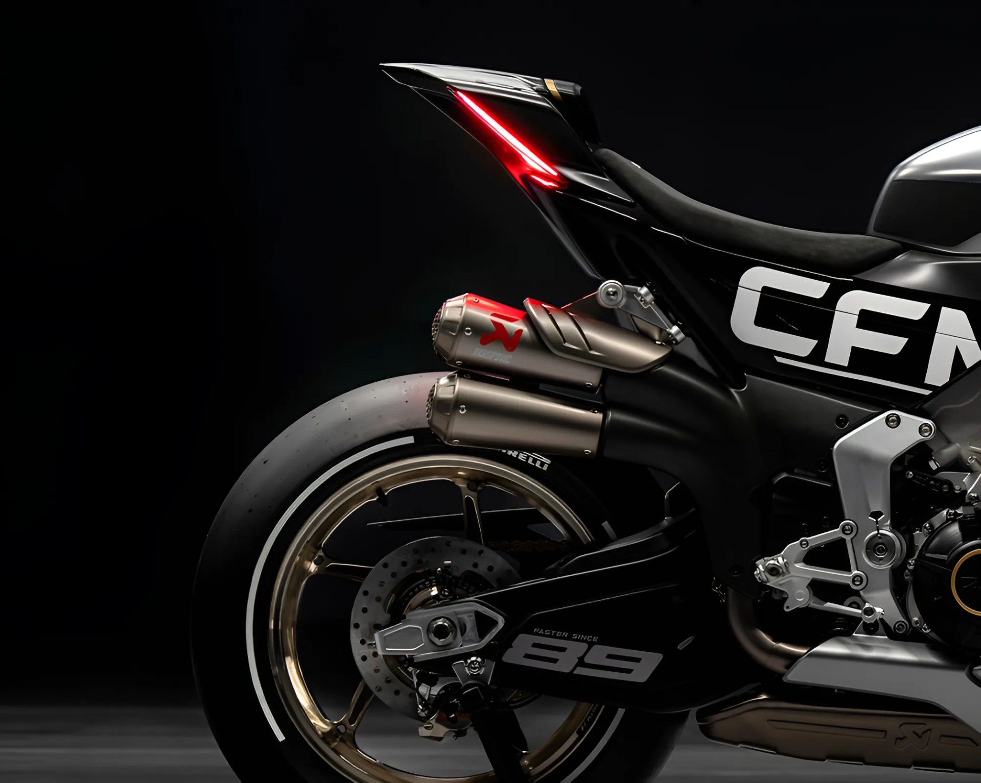 Close-up of the rear section of a black CFM motorcycle with gold rims, dual exhaust pipes, and a red taillight.