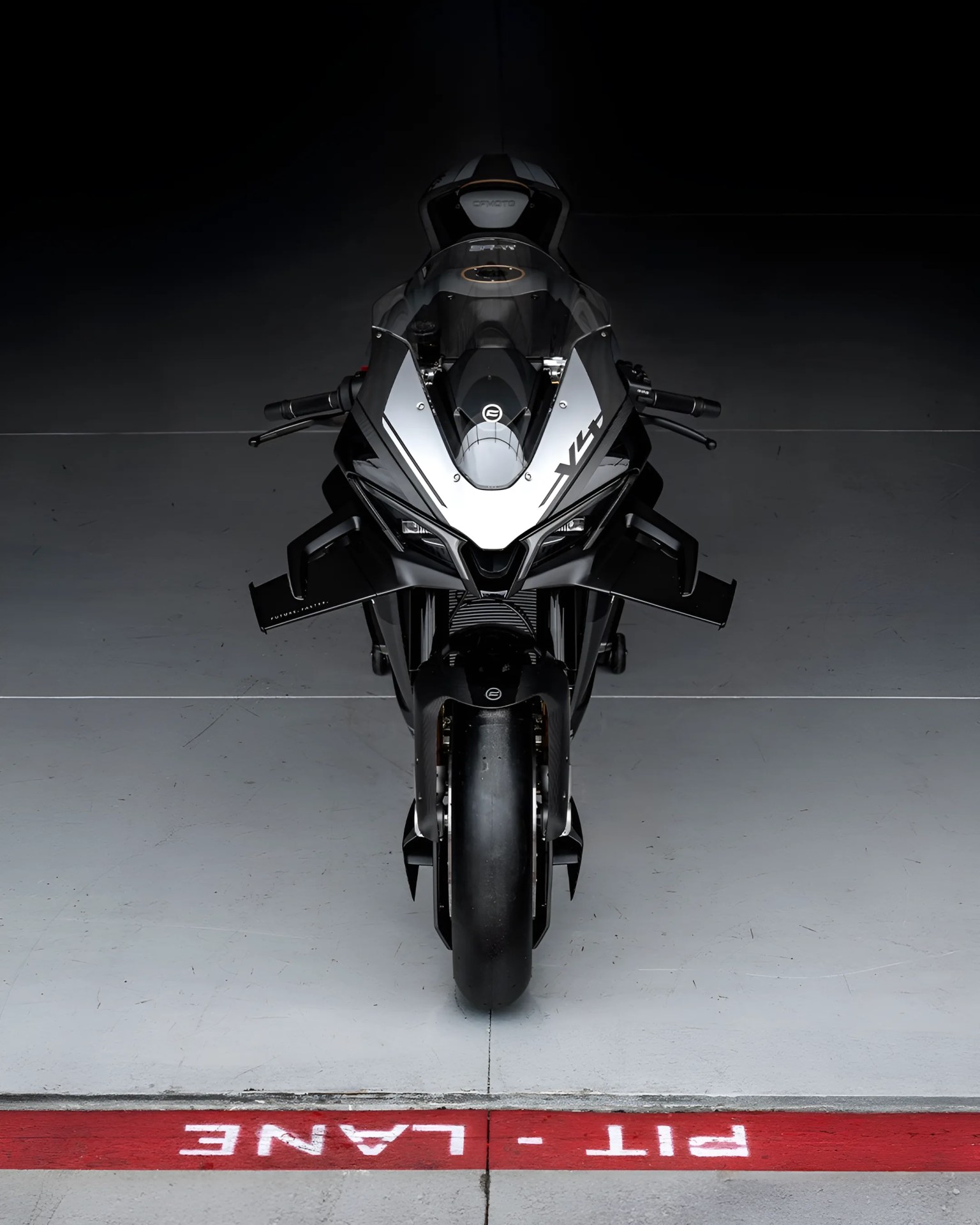 Front view of a black and silver sport motorcycle positioned on a gray floor with a red "PIT LANE" marking.