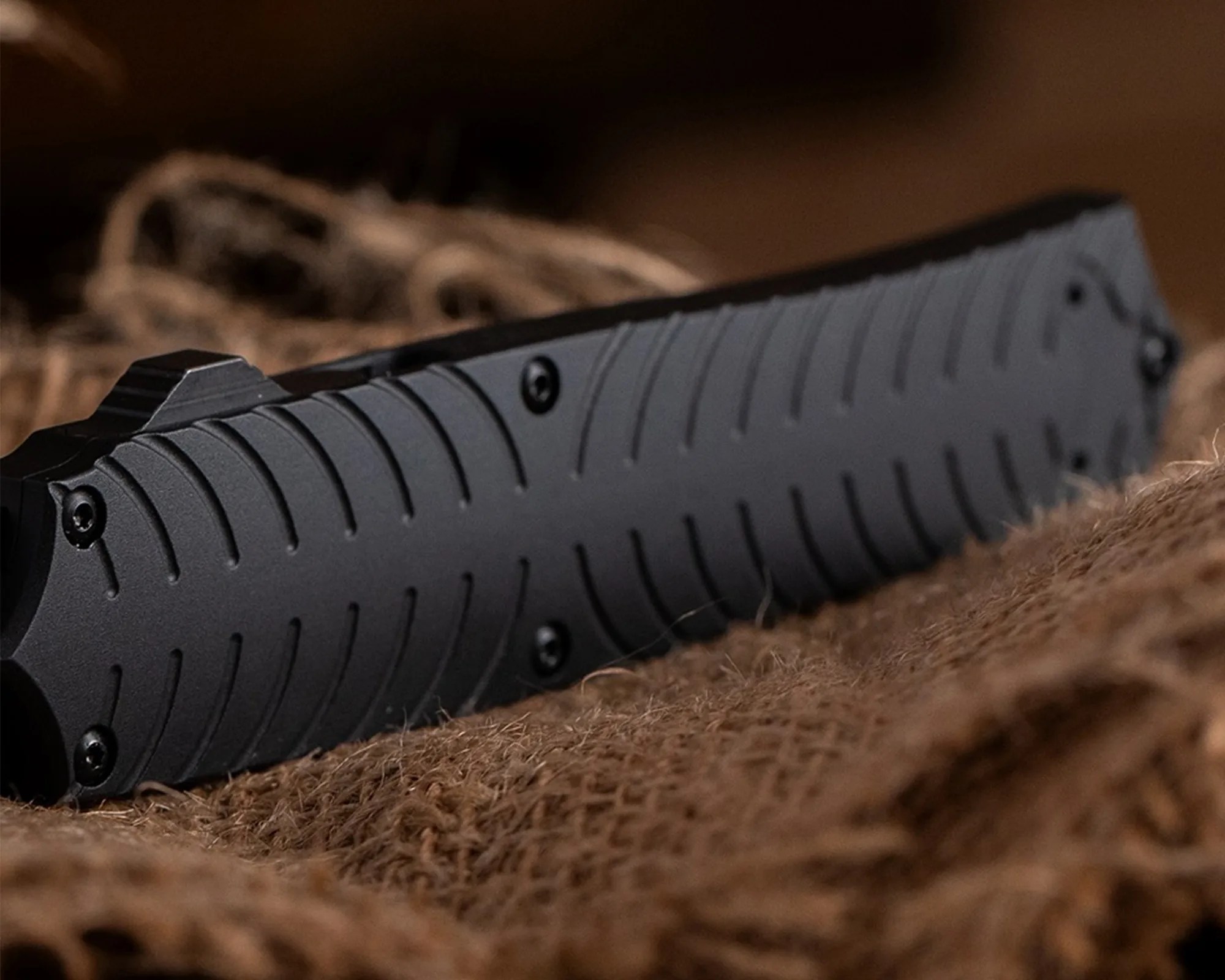Black textured handle of a folding knife resting on coarse brown fabric.
