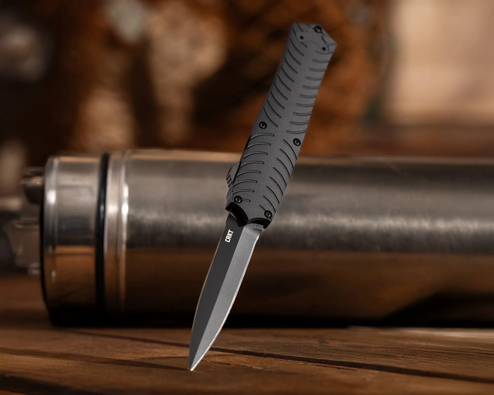 Black CRKT folding knife with textured handle standing blade-down on a wooden surface.
