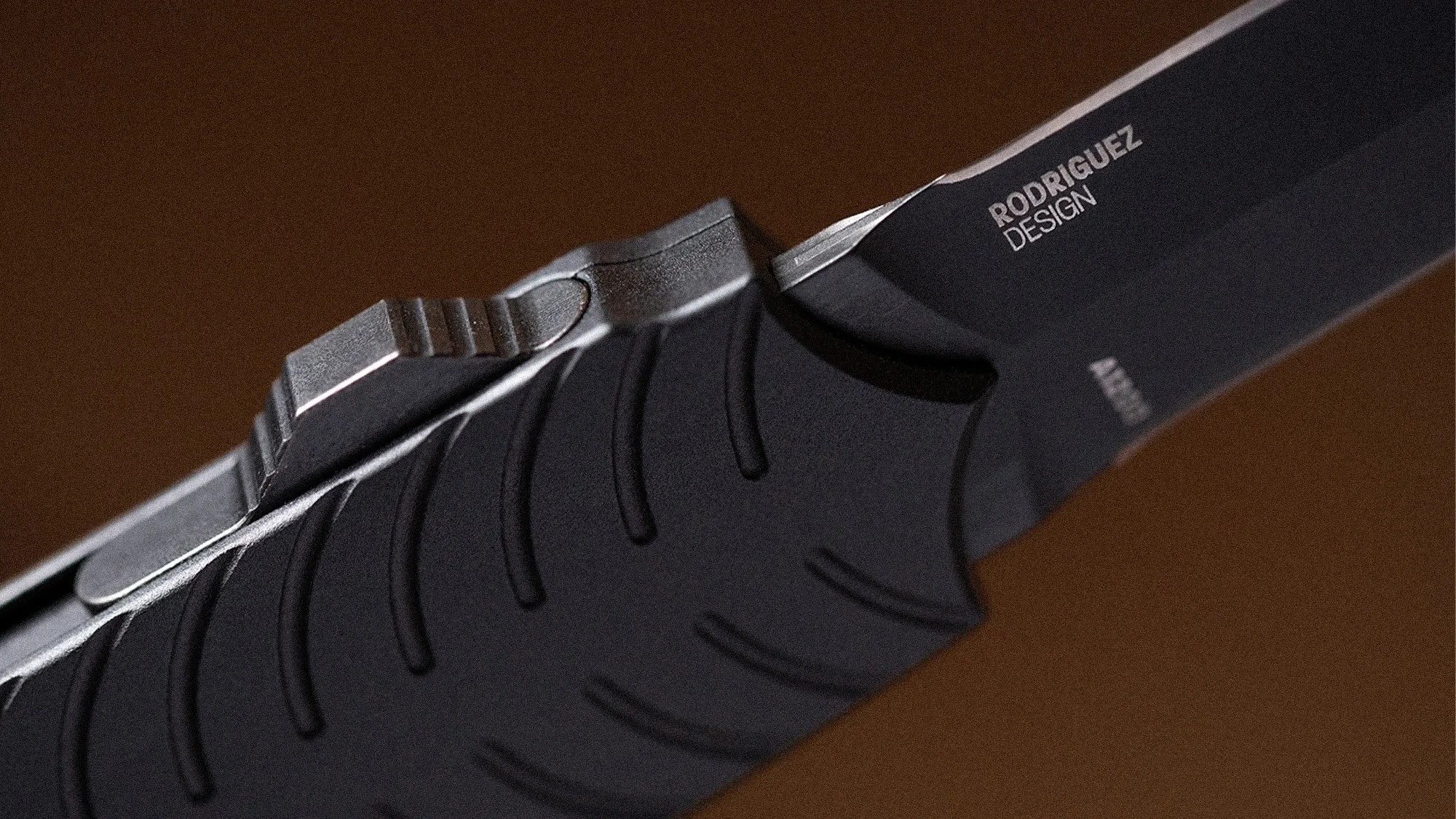 Close-up of a black folding knife handle with textured grip and partially visible blade marked "RODRIGUEZ DESIGN.