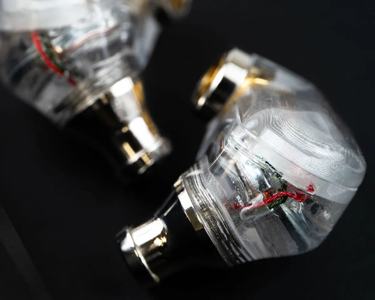 Pair of transparent in-ear monitor earphones with visible internal wiring on a black surface.