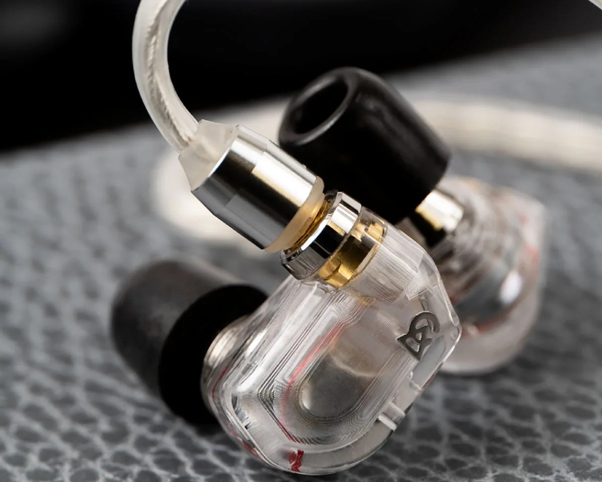 Transparent in-ear monitors with black ear tips and silver connectors on a textured surface.