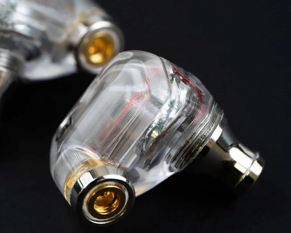 Transparent in-ear monitor housing with visible internal wiring and gold-plated connectors on a black background.