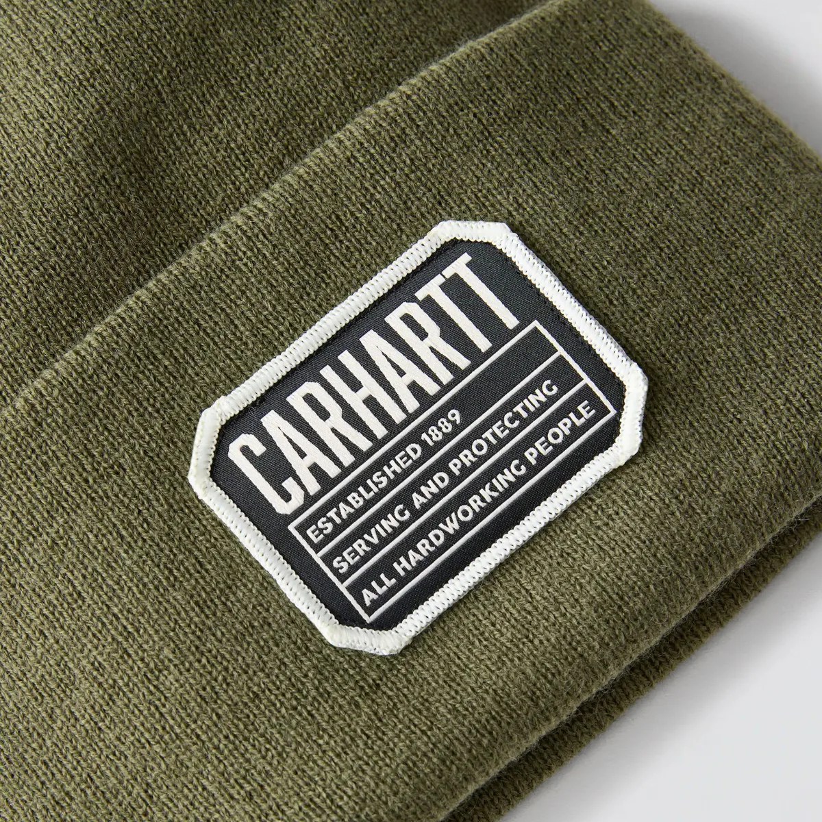 Olive green knit beanie with a black and white Carhartt logo patch sewn on the cuff.
