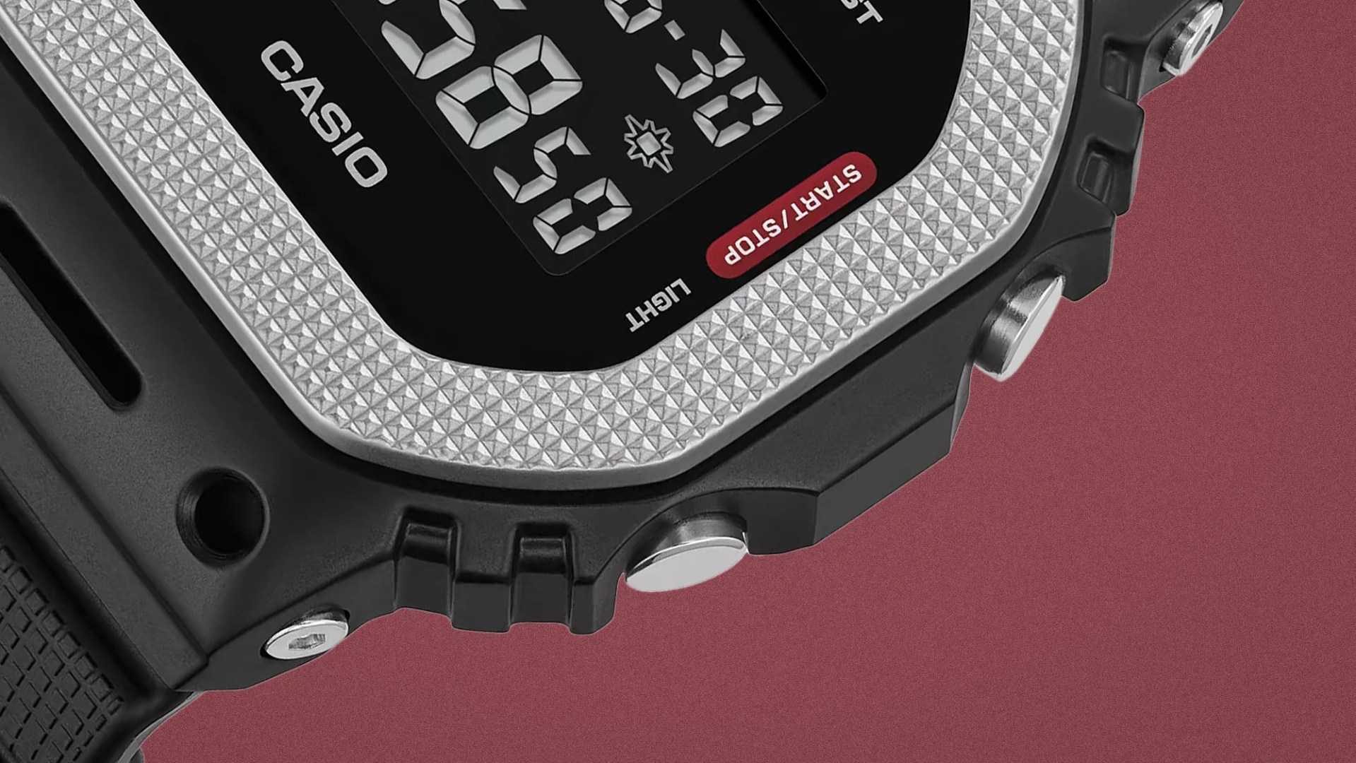 Close-up of a Casio digital watch with a textured silver bezel and black resin case on a maroon background.