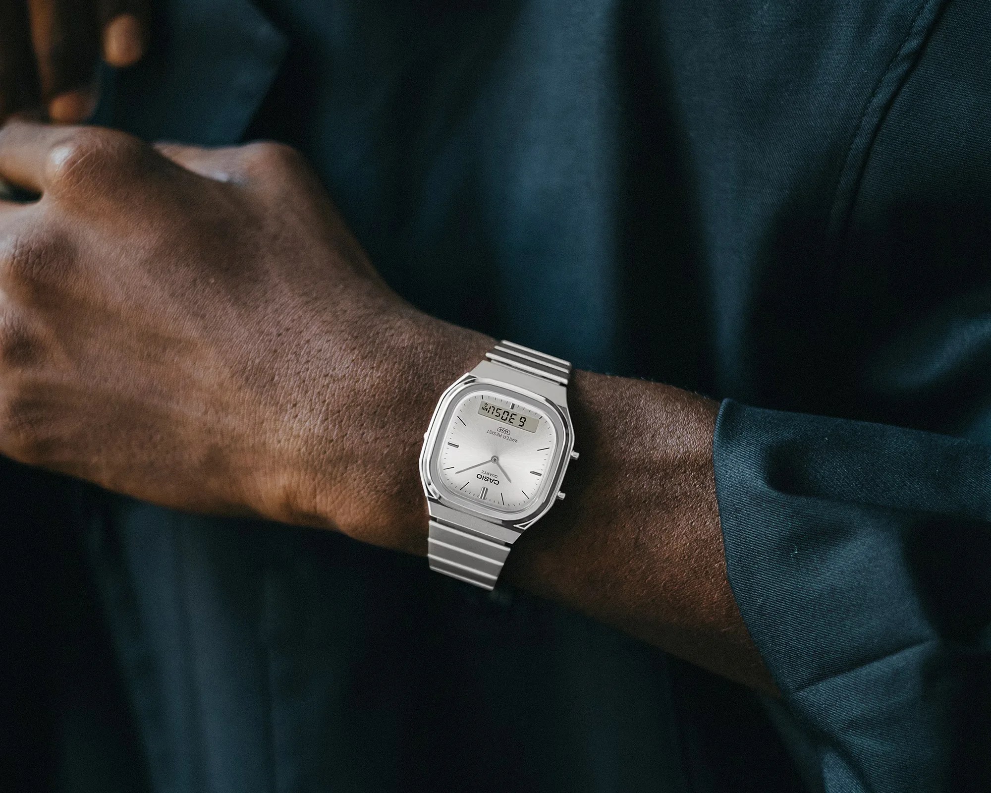 Silver Casio wristwatch with analog and digital display on a wrist wearing a dark long-sleeve shirt.