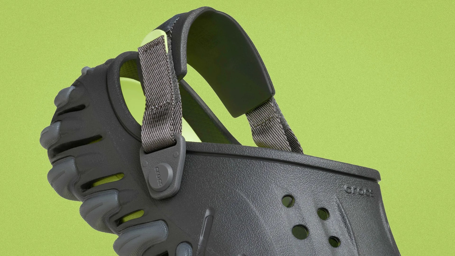 Black Crocs clog with rugged sole and adjustable heel strap against a green background.