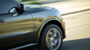 Glossy dark green SUV front side with a yellow Hellcat emblem and spinning front wheel on a road.