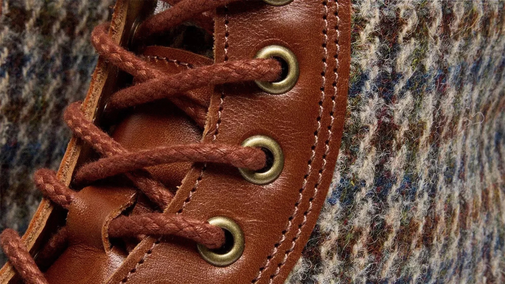 Close-up of brown leather shoe eyelets with brown laces and multicolored wool fabric.