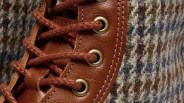 Close-up of brown leather shoe eyelets with brown laces and multicolored wool fabric.