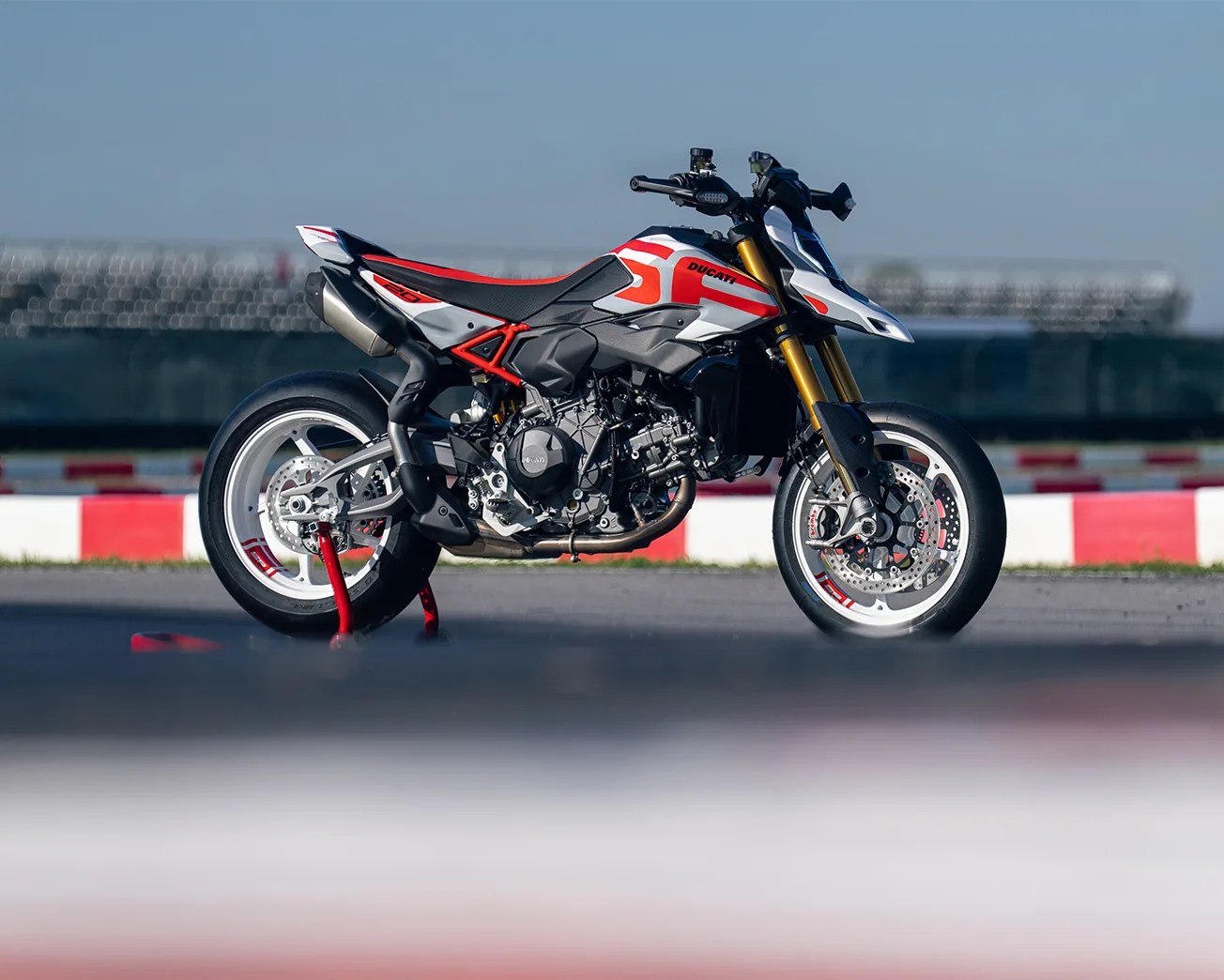 White and red Ducati motorcycle with gold front forks on a racetrack.