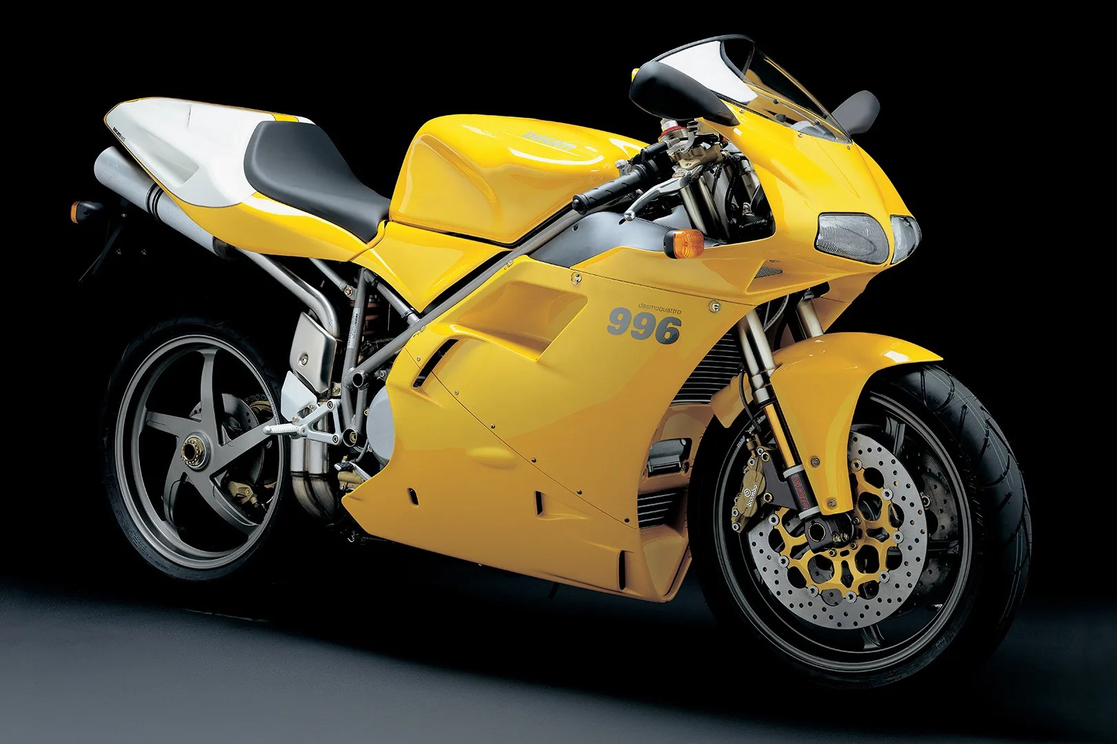 Yellow Ducati 996 sport motorcycle with black seat and silver wheels on a dark background.