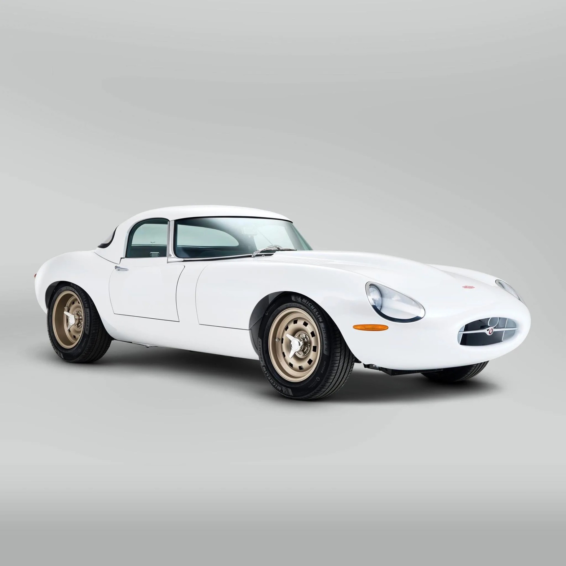White classic sports car with beige wheels and a sleek, aerodynamic design on a gray background.
