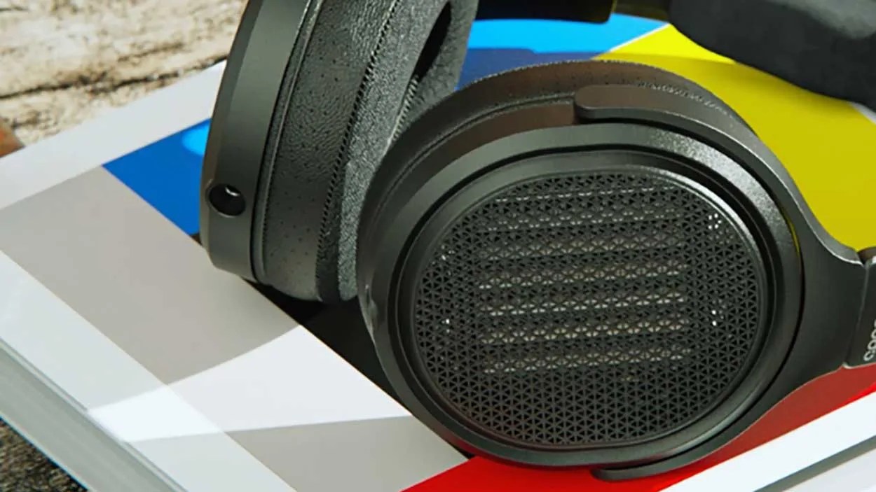 Black over-ear headphones with mesh speaker grills resting on a colorful book with blue, yellow, red, and gray sections.