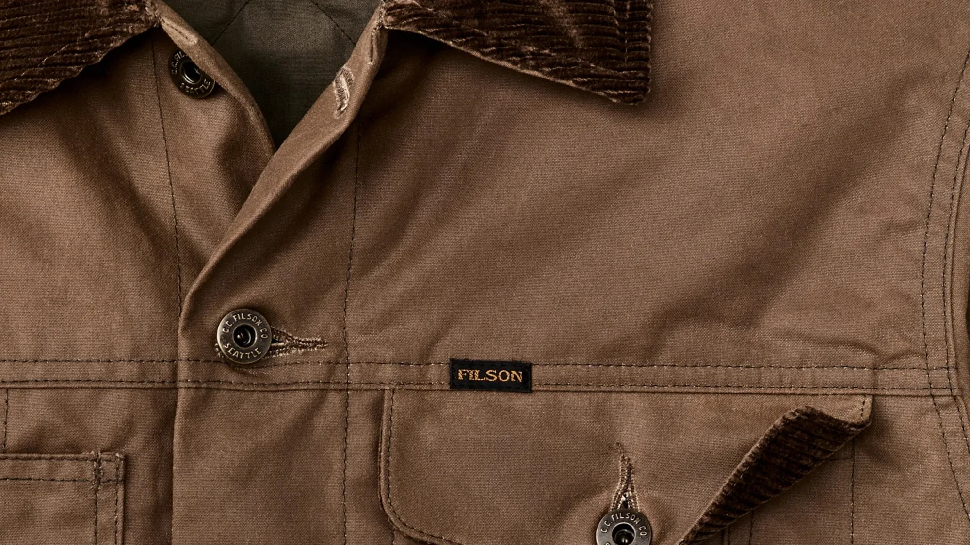 Brown Filson jacket with corduroy collar and black buttons with "C.C. Filson Co Seattle" text.