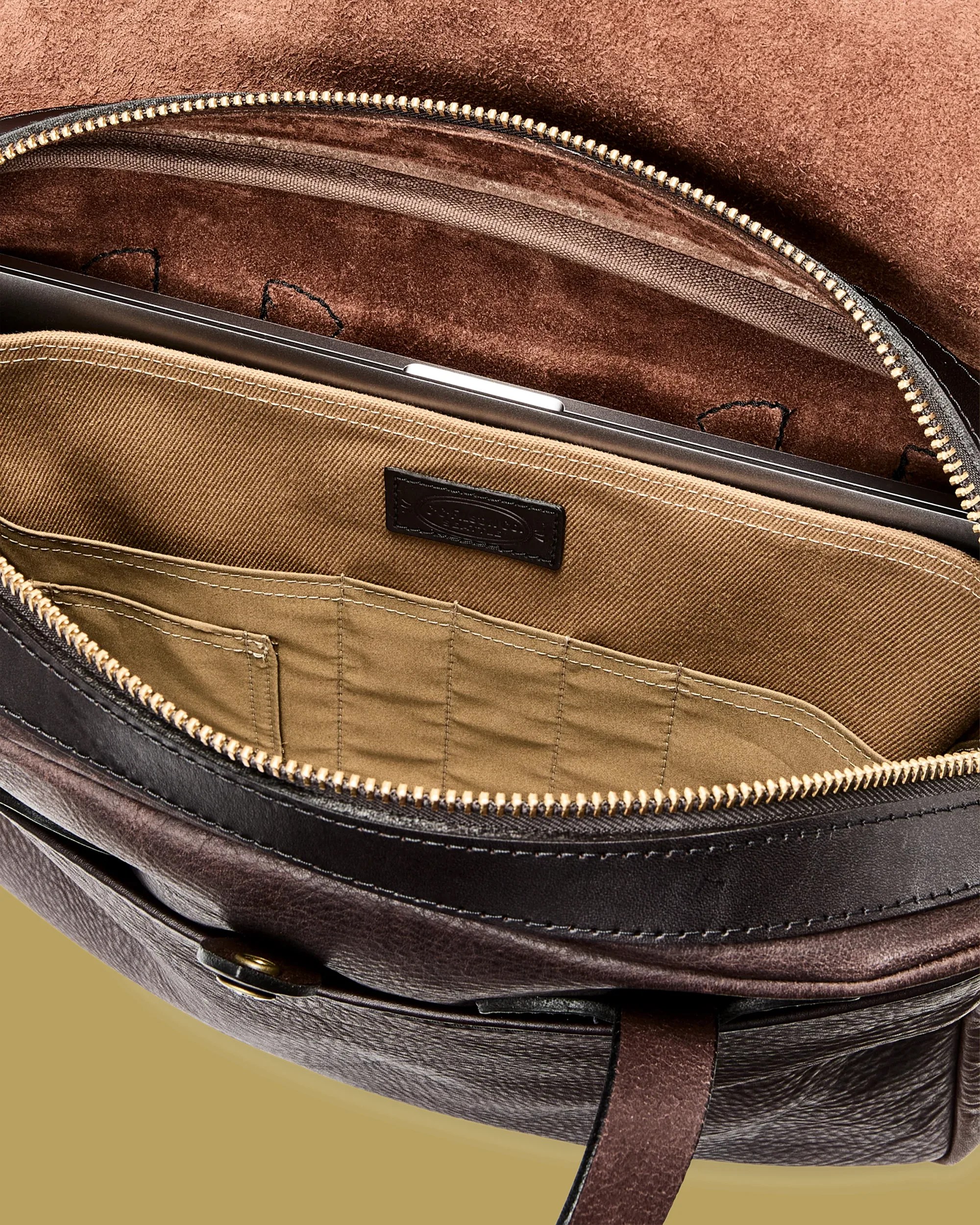Dark brown leather bag with a tan fabric interior pocket holding a laptop.