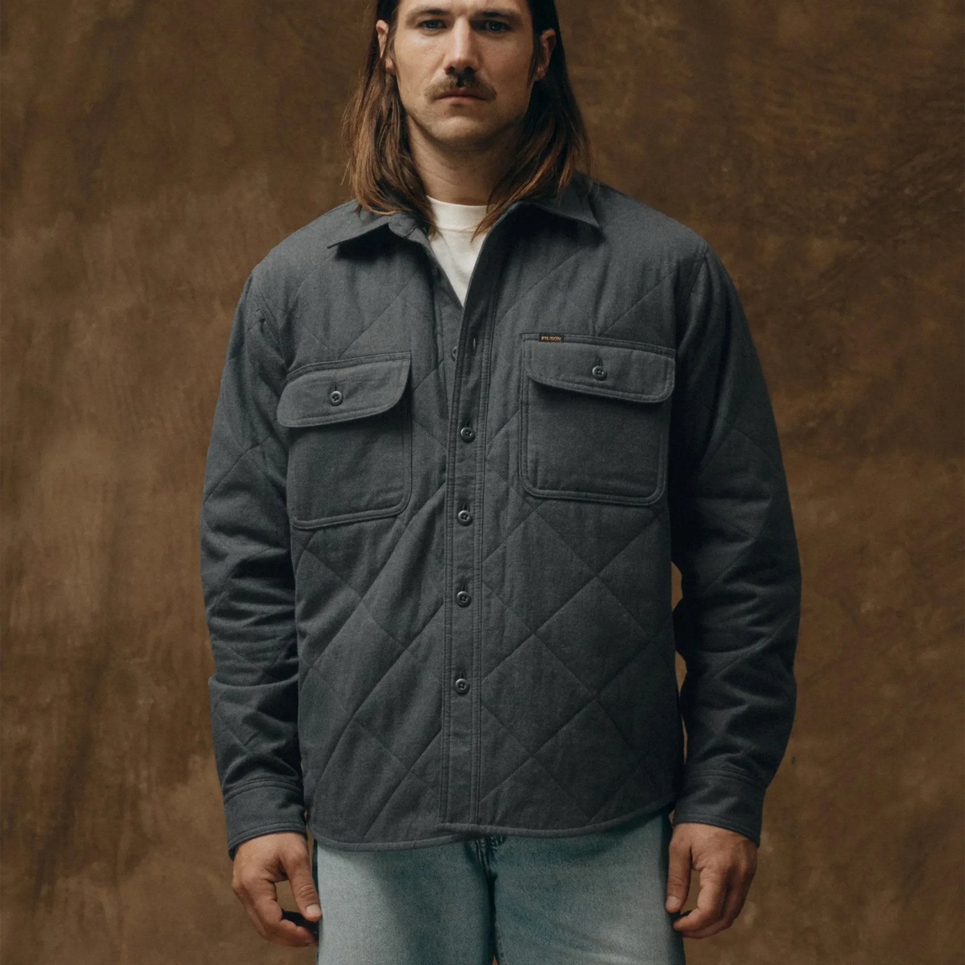 Dark gray quilted button-up jacket with two buttoned chest pockets worn by a person.