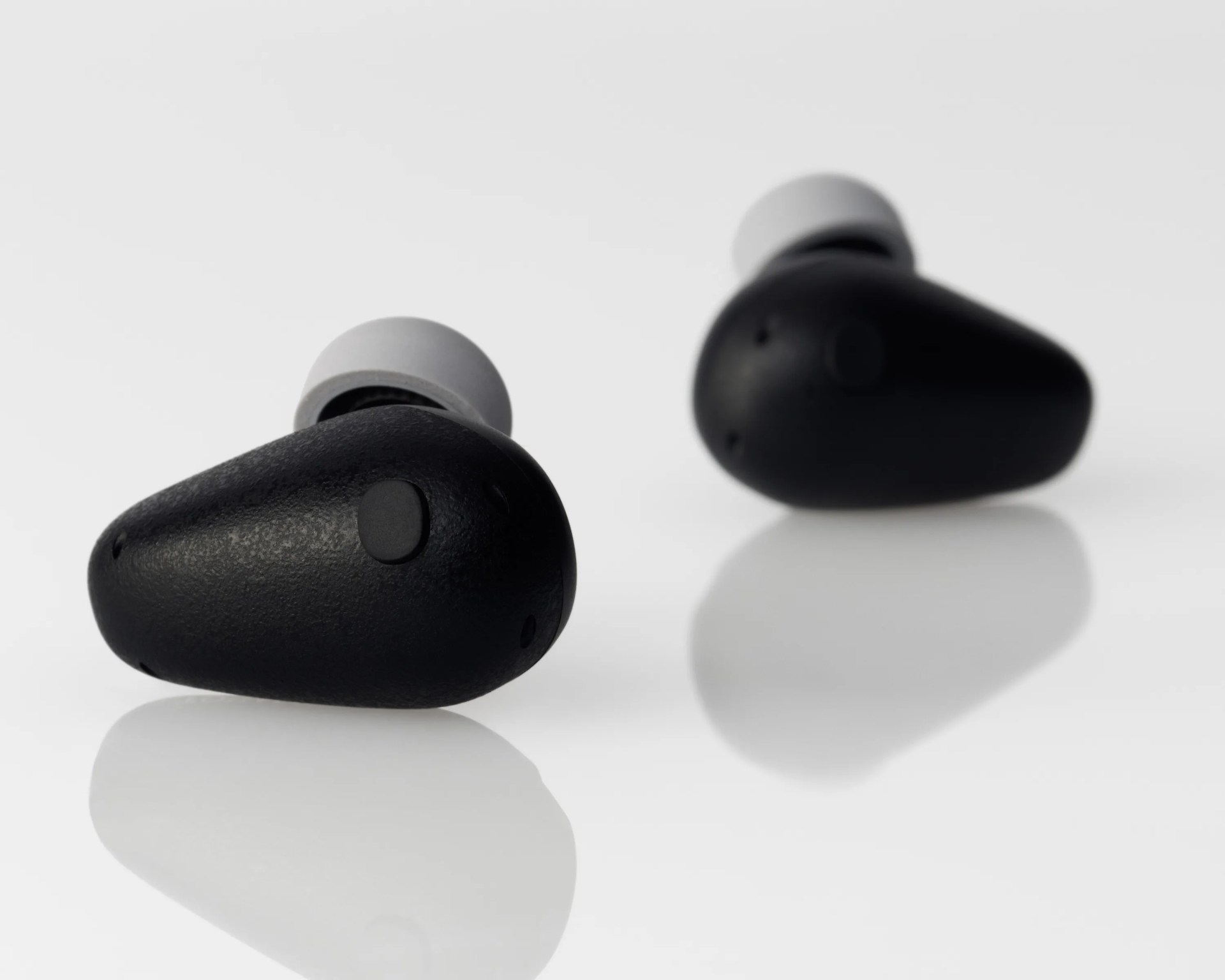Pair of black wireless earbuds with gray silicone ear tips on a reflective white surface.