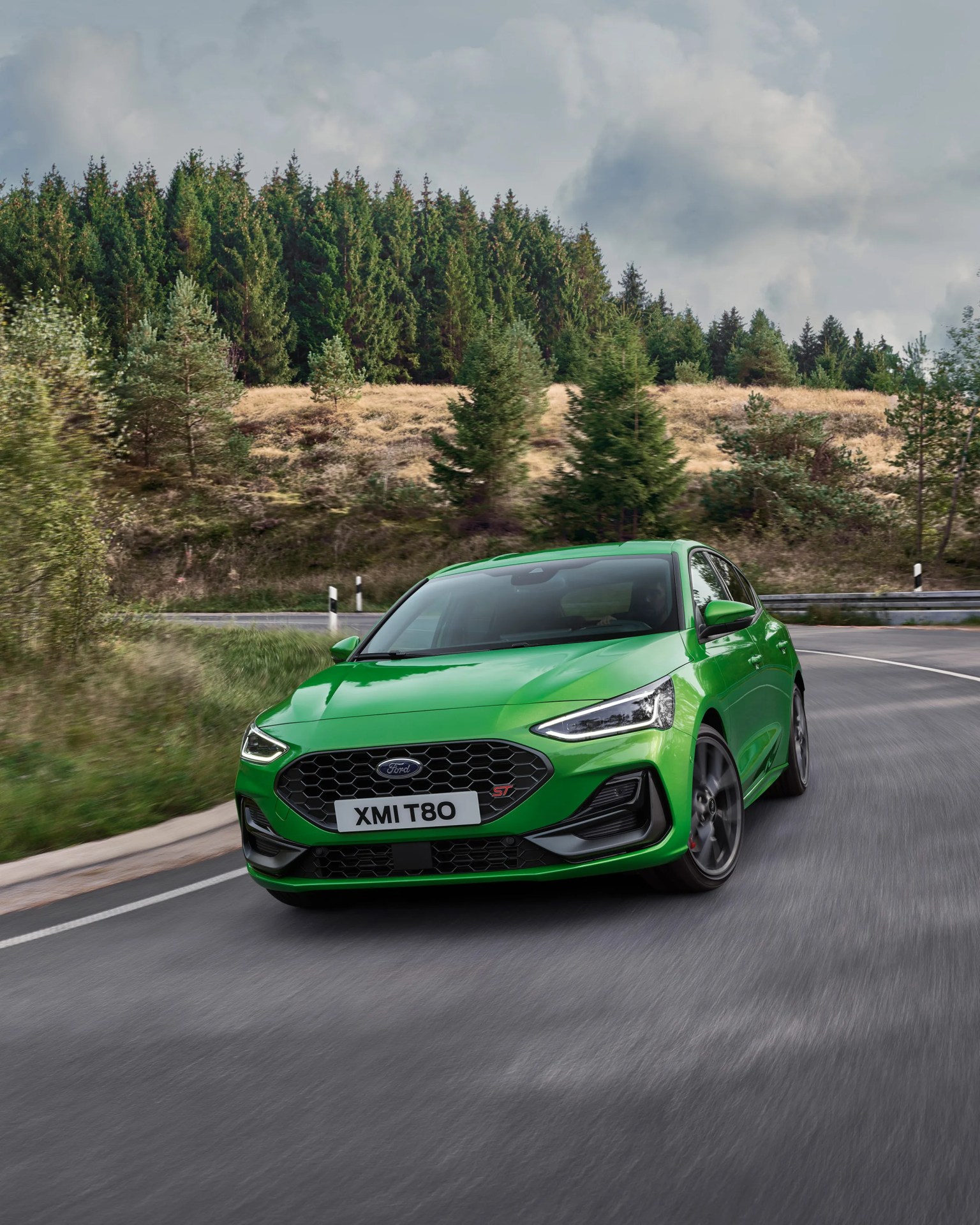 Bright green Ford hatchback car driving on a curved road with trees in the background.