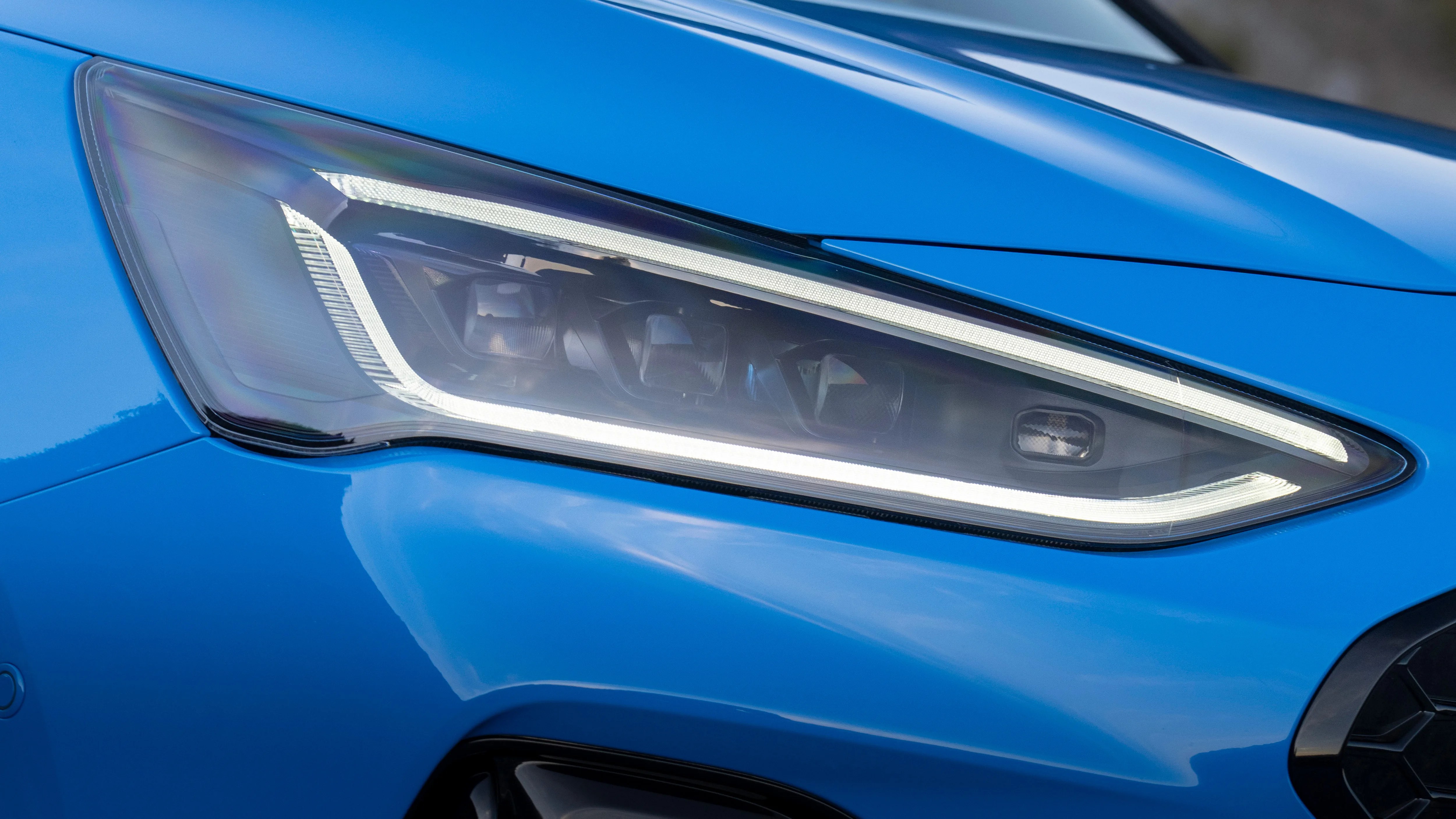 Close-up of a sleek blue car's modern LED headlight with a sharp, angular design.