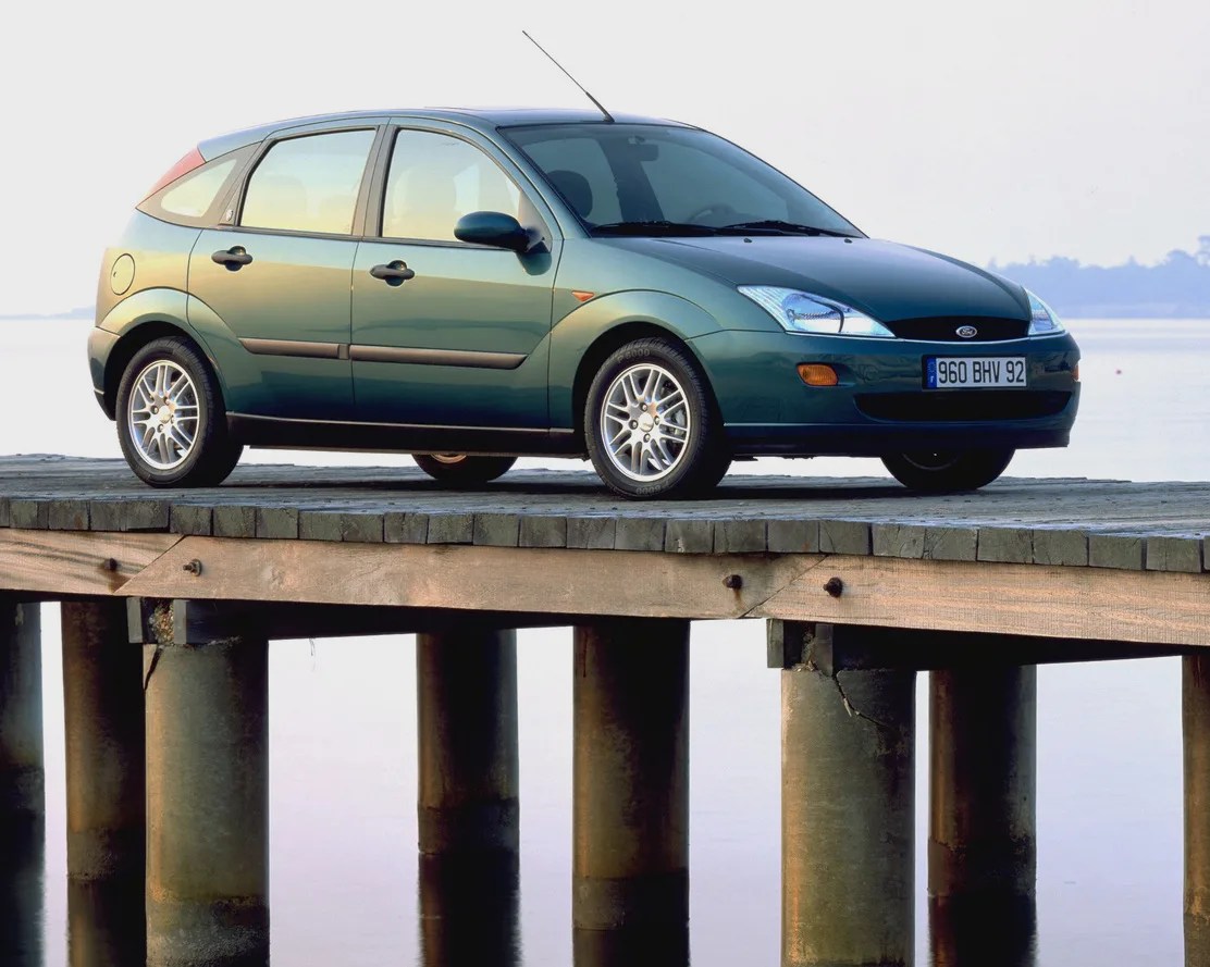 Green Ford Focus hatchback parked on a wooden pier over calm water.