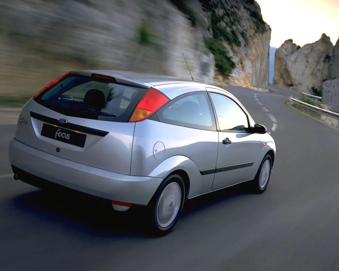 Silver Ford Focus hatchback driving on a winding mountain road near rocky cliffs.