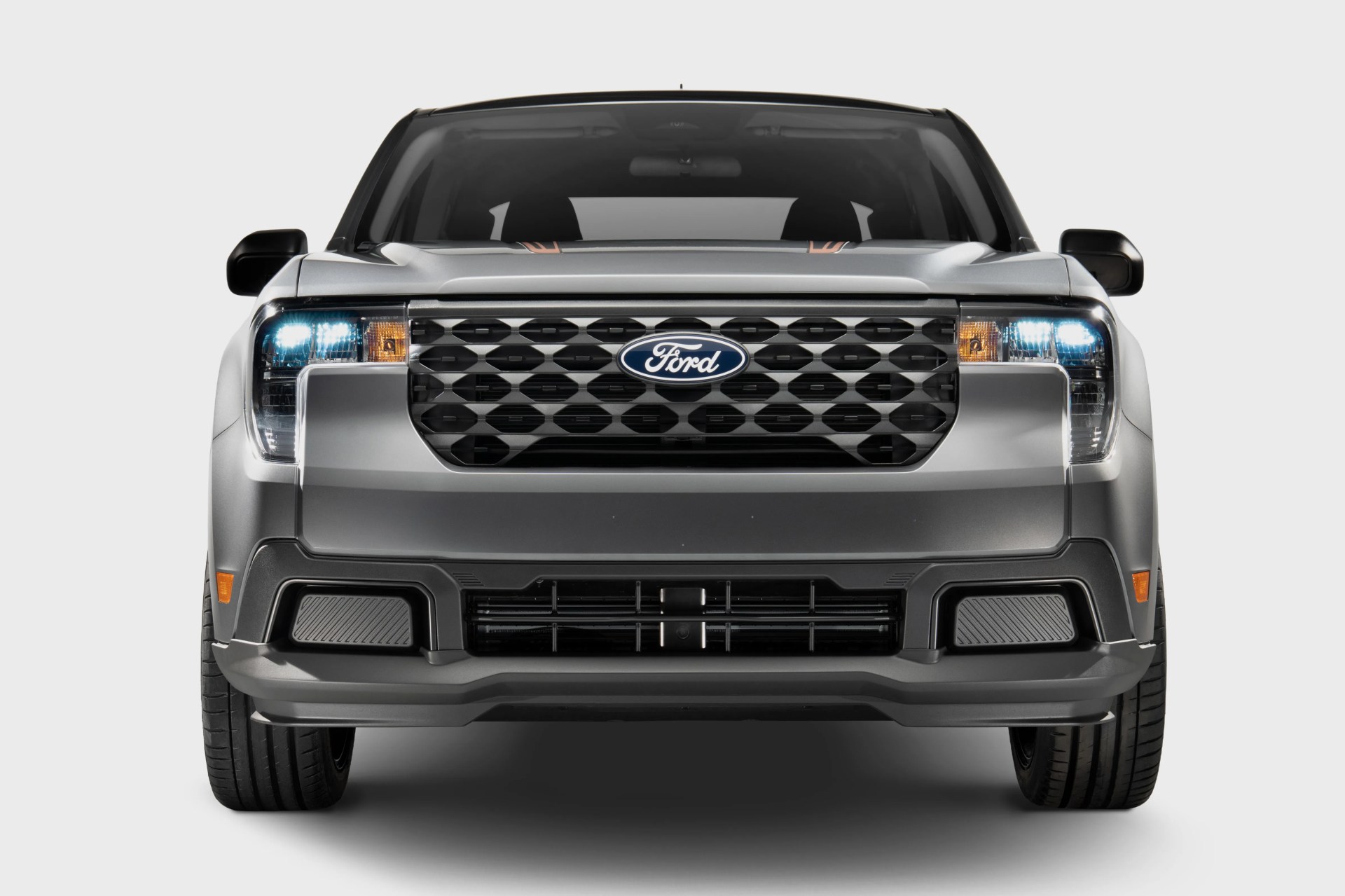 Front view of a silver Ford electric pickup truck with illuminated headlights and a black grille.