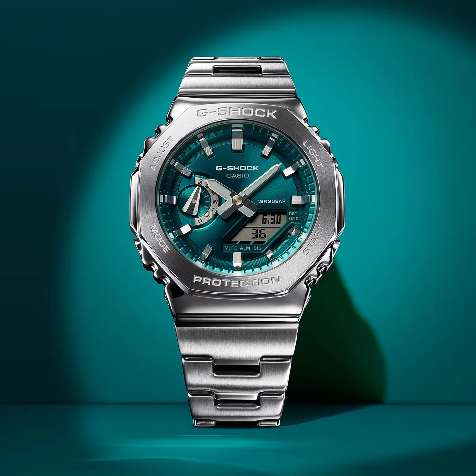 Silver stainless steel G-Shock Casio watch with teal dial and digital display on teal background.