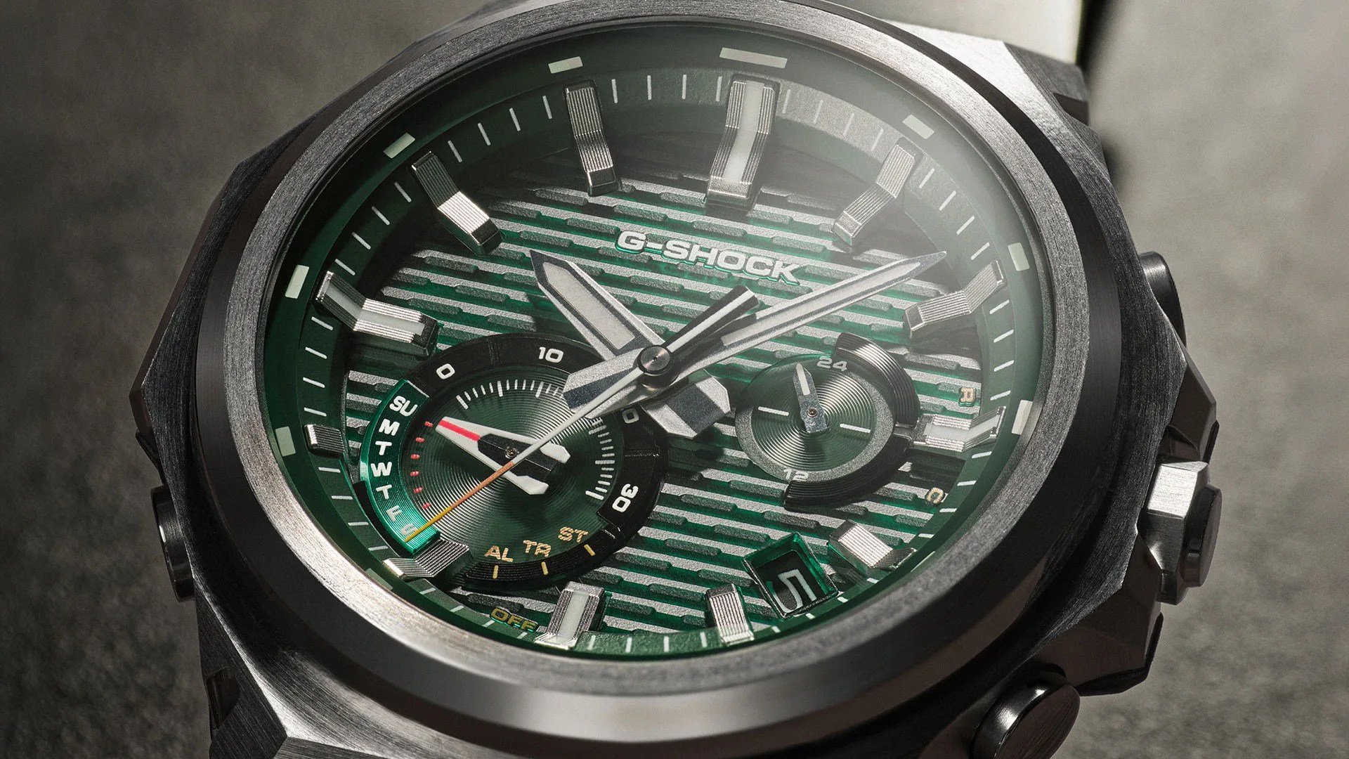 Close-up of a G-Shock watch with a green textured dial, silver hour markers, and multiple subdials in a metal case.