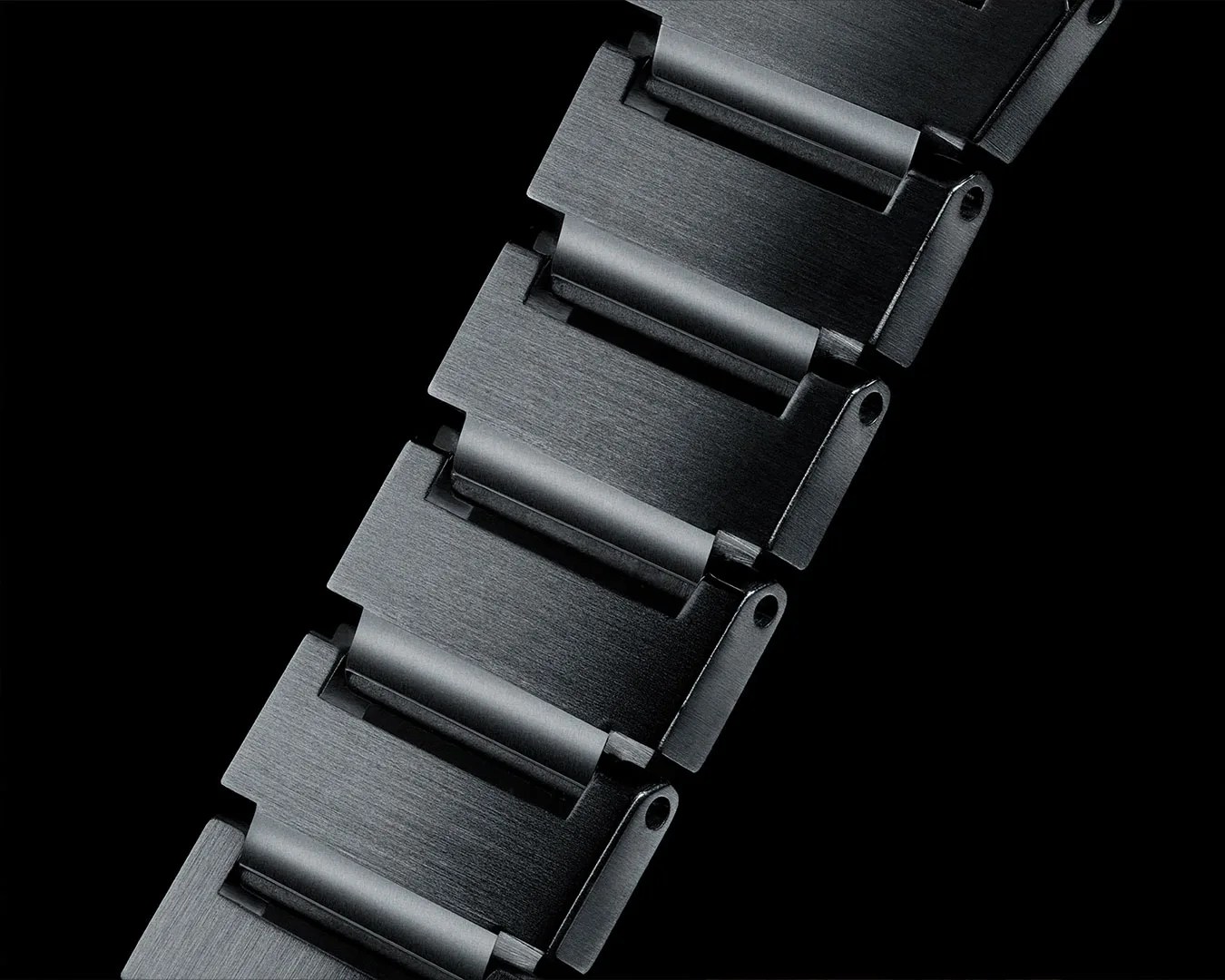 Close-up of a black brushed metal watch band with rectangular links on a black background.