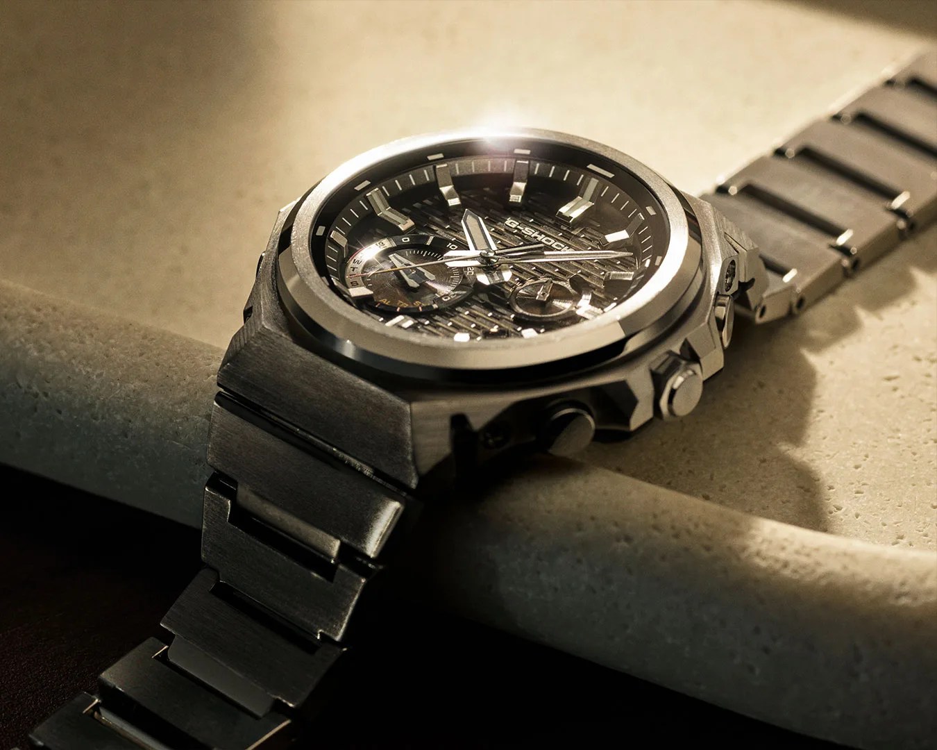 Black metal G-Shock wristwatch with textured dial and chronograph subdials on a stone surface.
