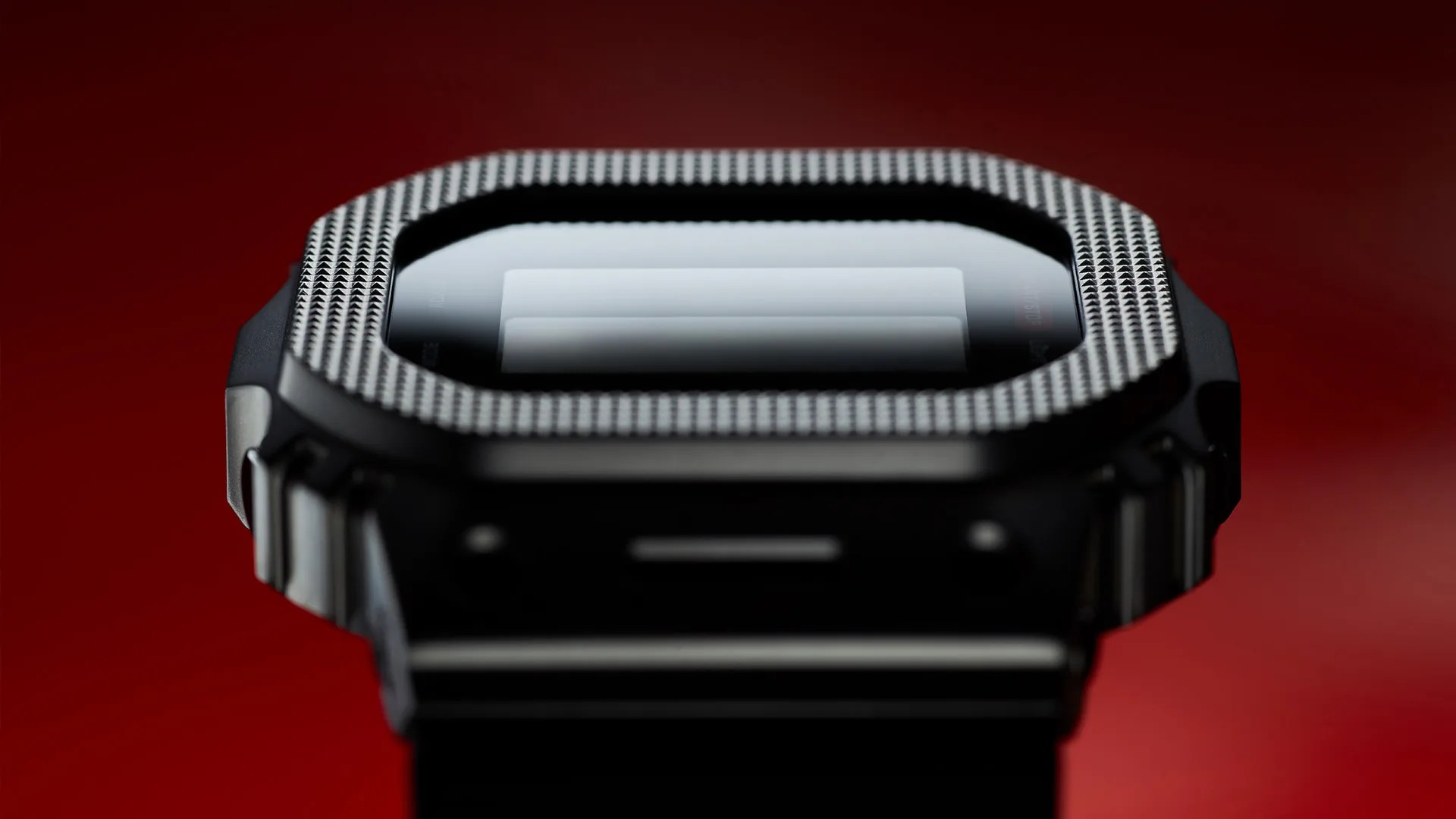 Close-up of a black digital watch with a textured bezel and reflective screen against a red background.