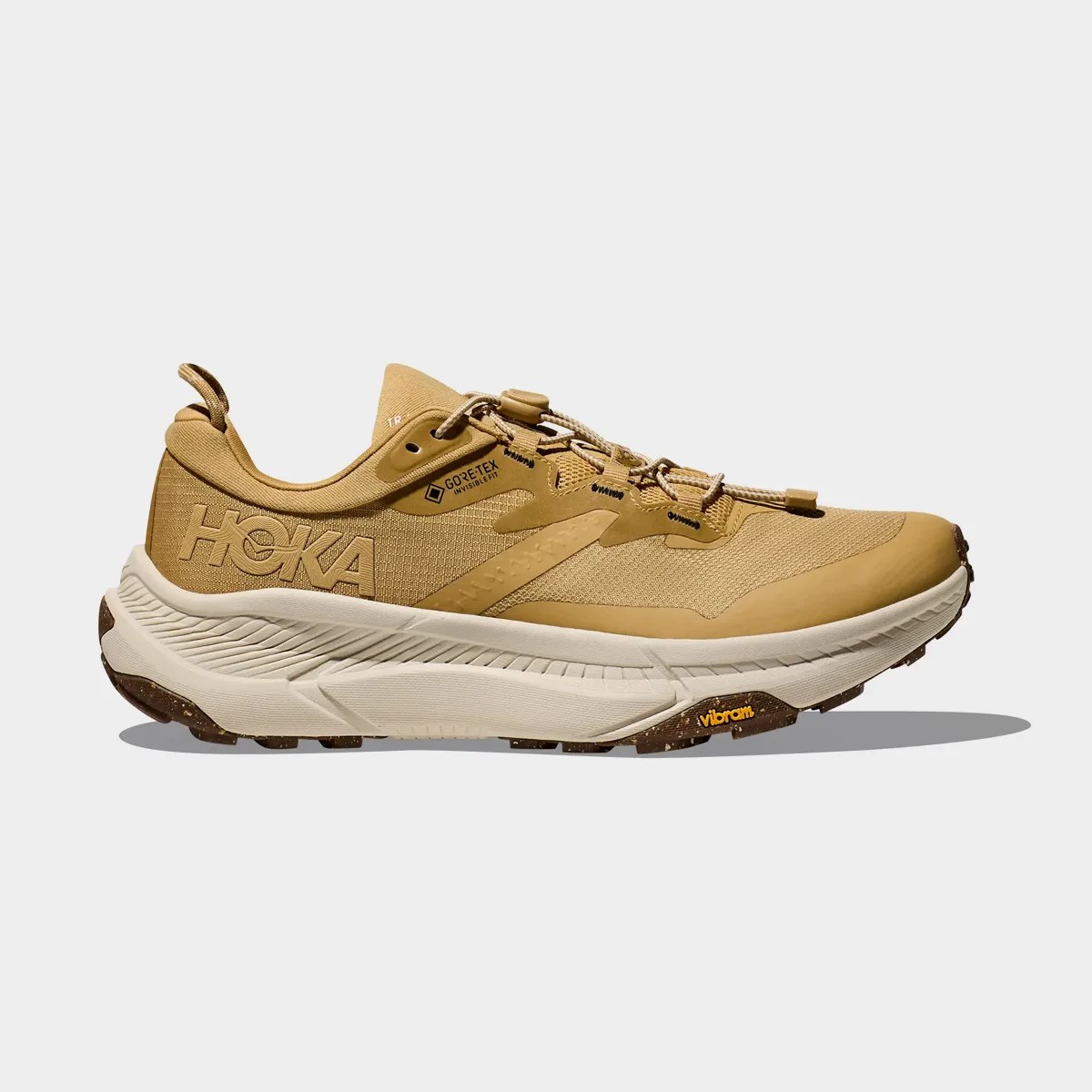 Tan Hoka running shoe with white midsole and Vibram outsole on a gray background.