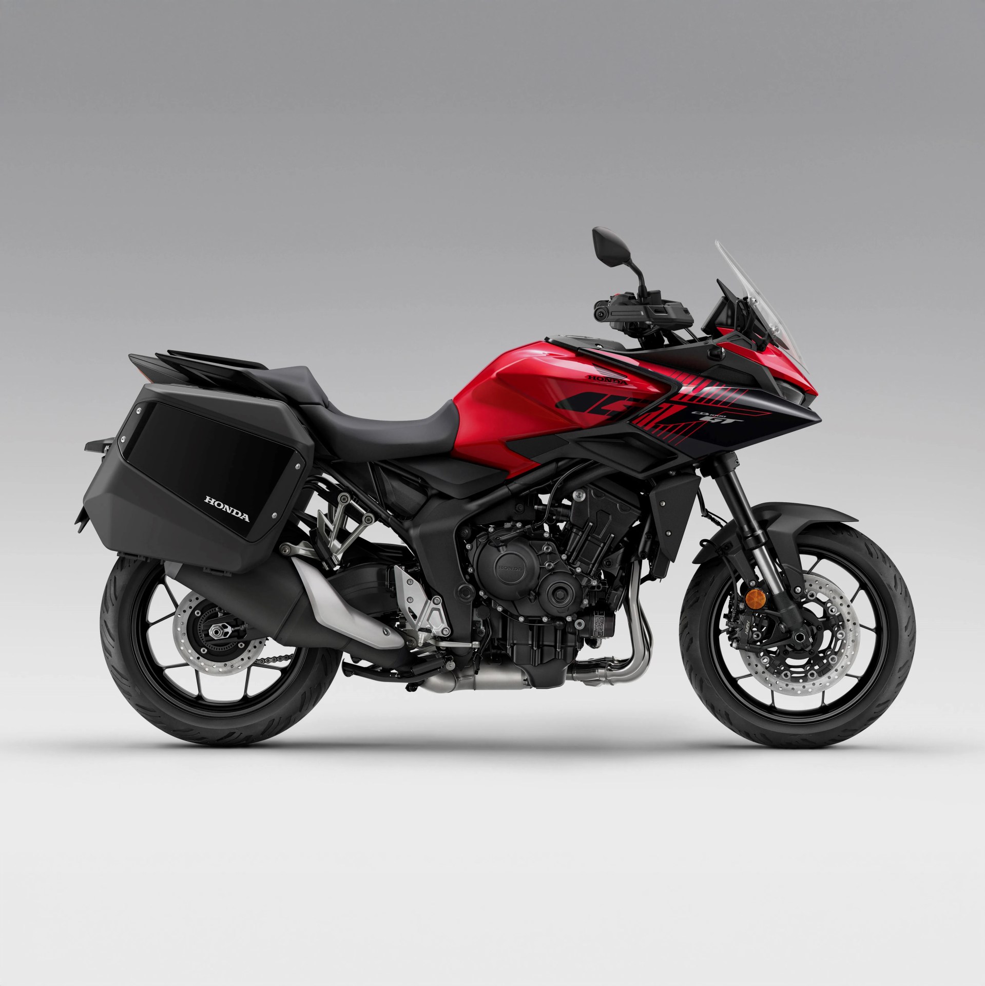 Red and black Honda sport touring motorcycle with side panniers and windshield on a gray background.