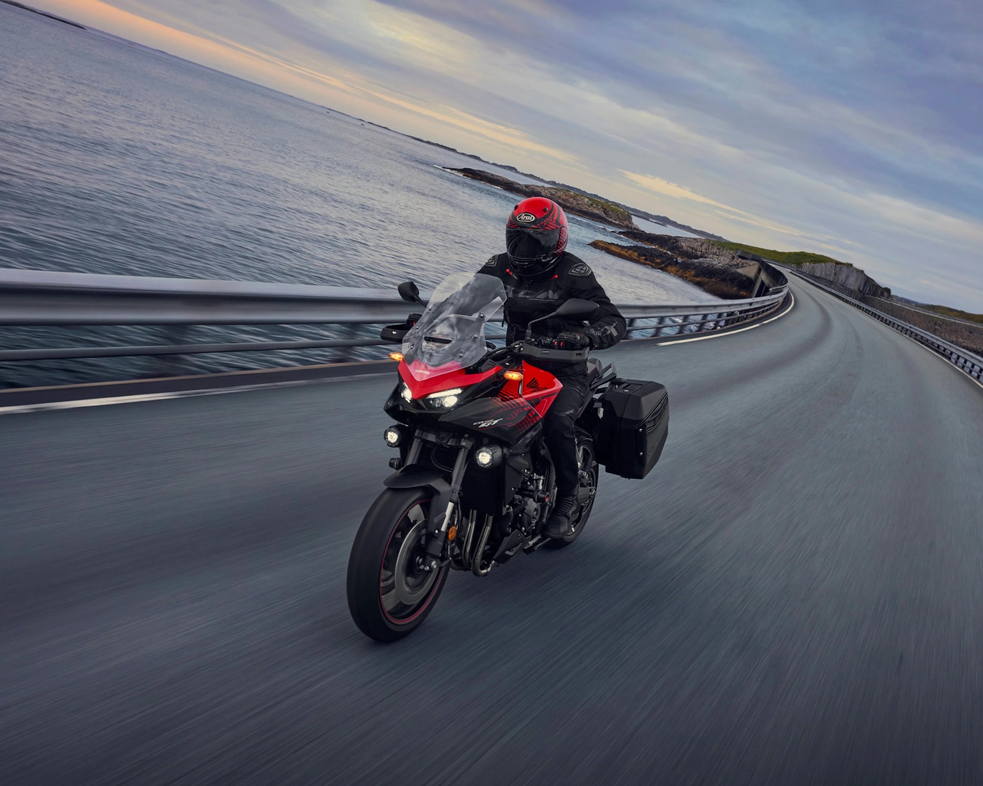 Black and red Honda motorcycle with side panniers ridden on a coastal road with guardrails.