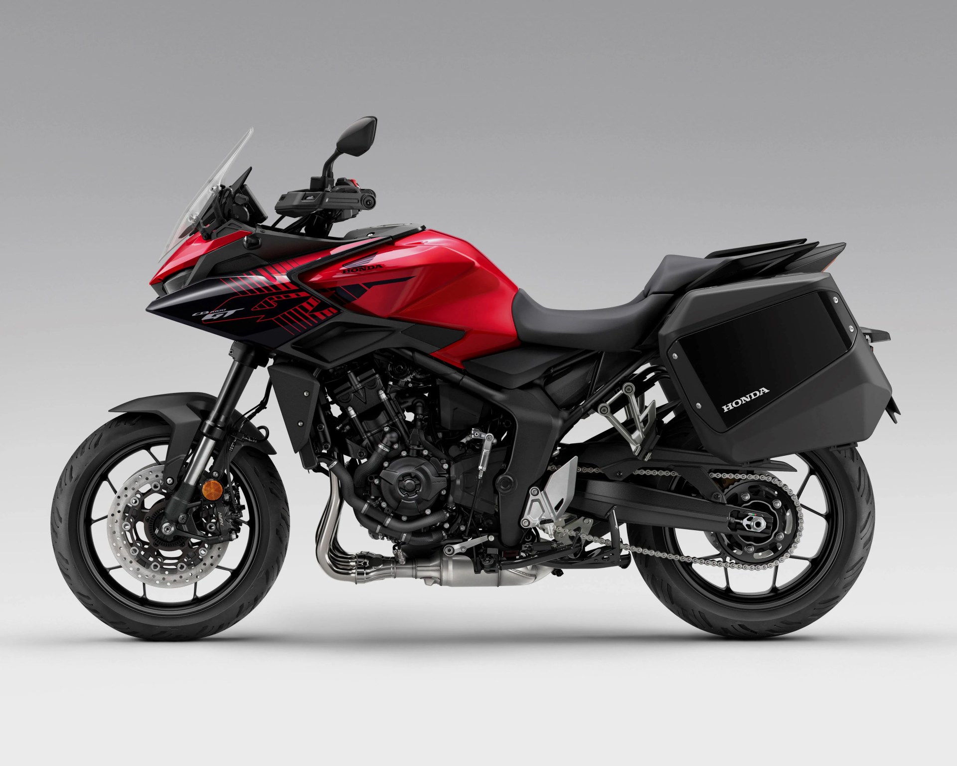 Red and black Honda touring motorcycle with side panniers and a clear windshield on a gray background.