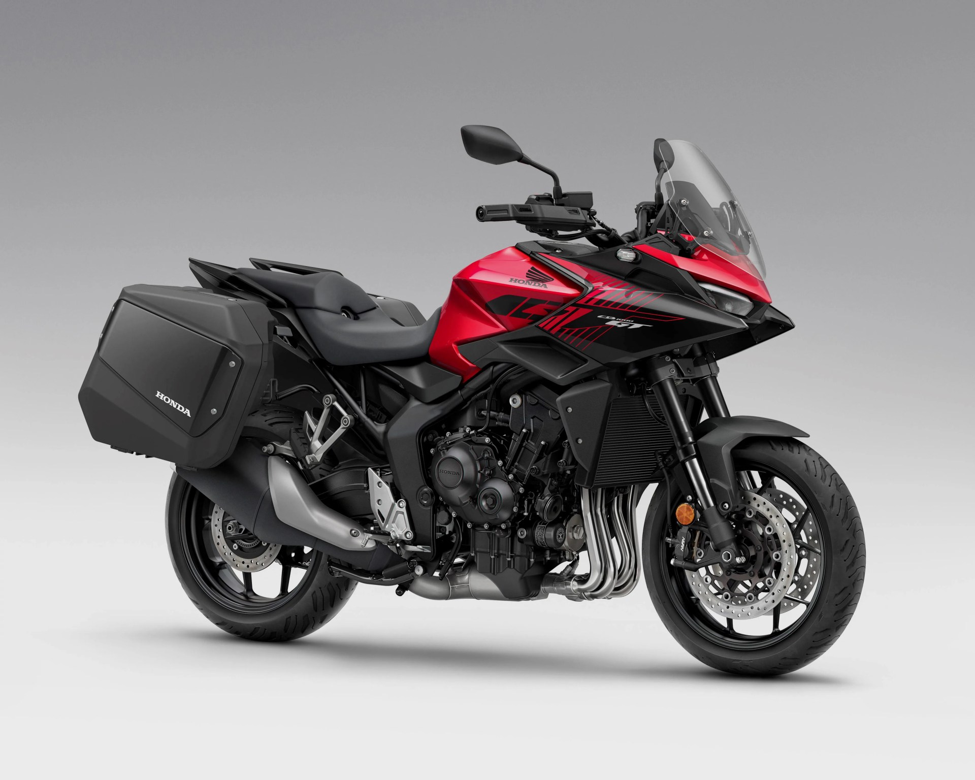 Red and black Honda touring motorcycle with side panniers and a clear windshield on a gray background.