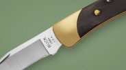 Close-up of a Buck 088 folding knife blade and brass bolster with dark wooden handle on a green background.