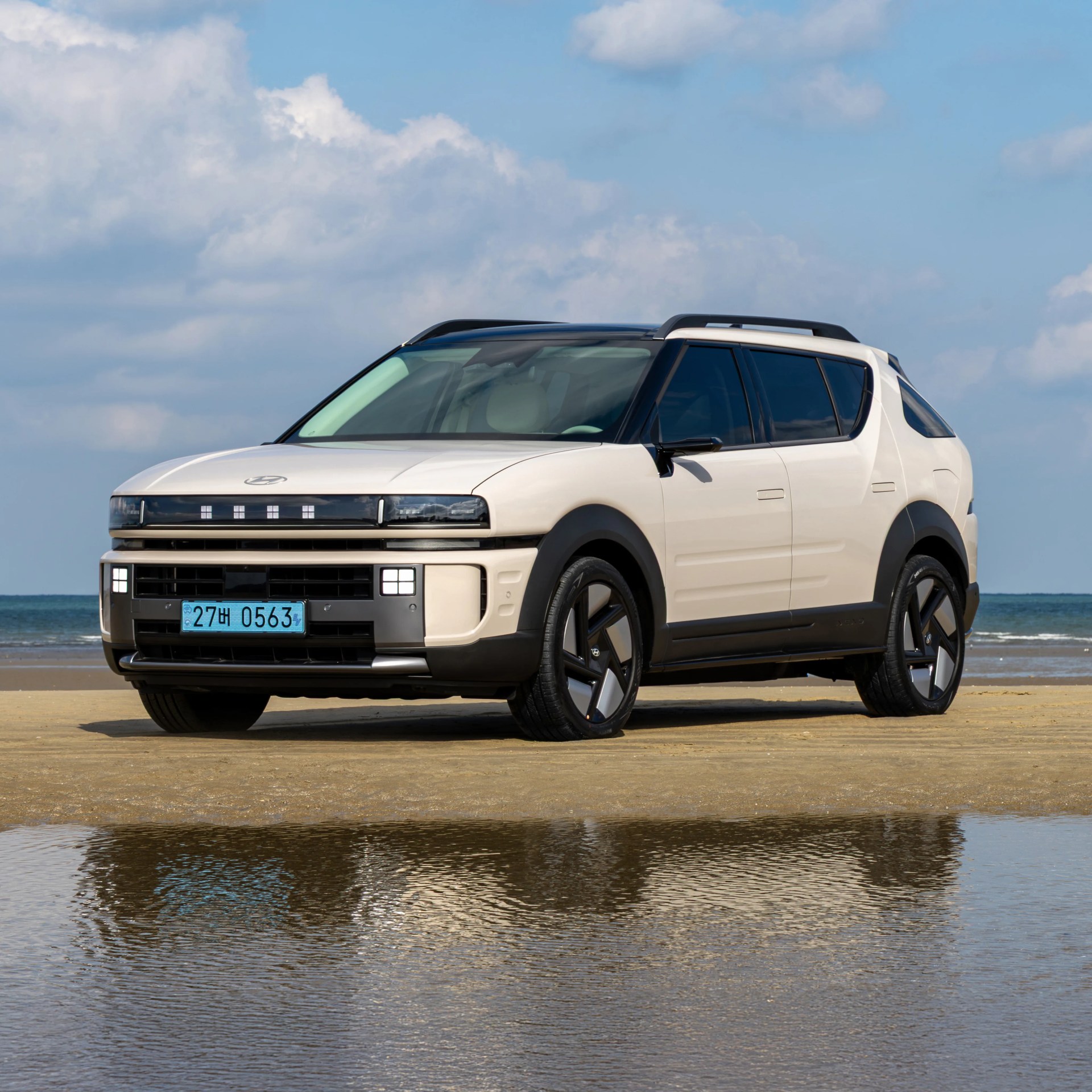 Beige Hyundai Ioniq 5 electric SUV parked on a sandy beach with ocean and blue sky in the background.