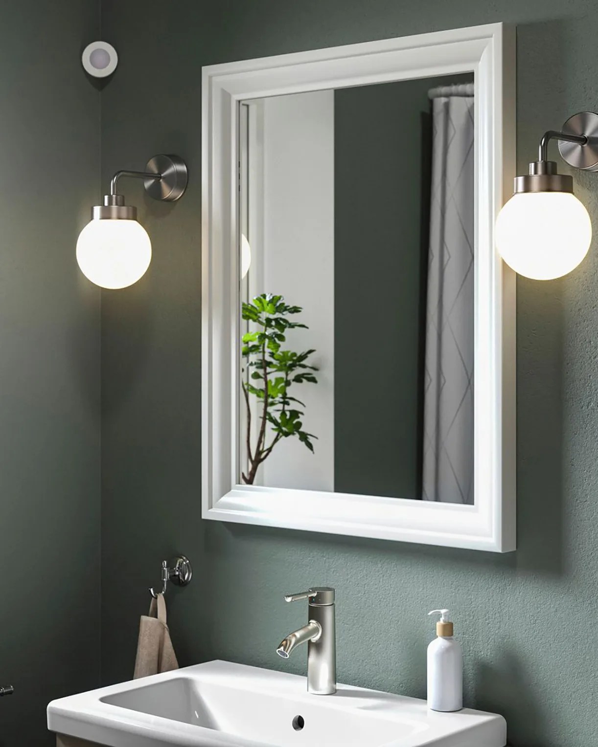 White-framed rectangular mirror above white sink with brushed metal faucet and two round wall sconces.