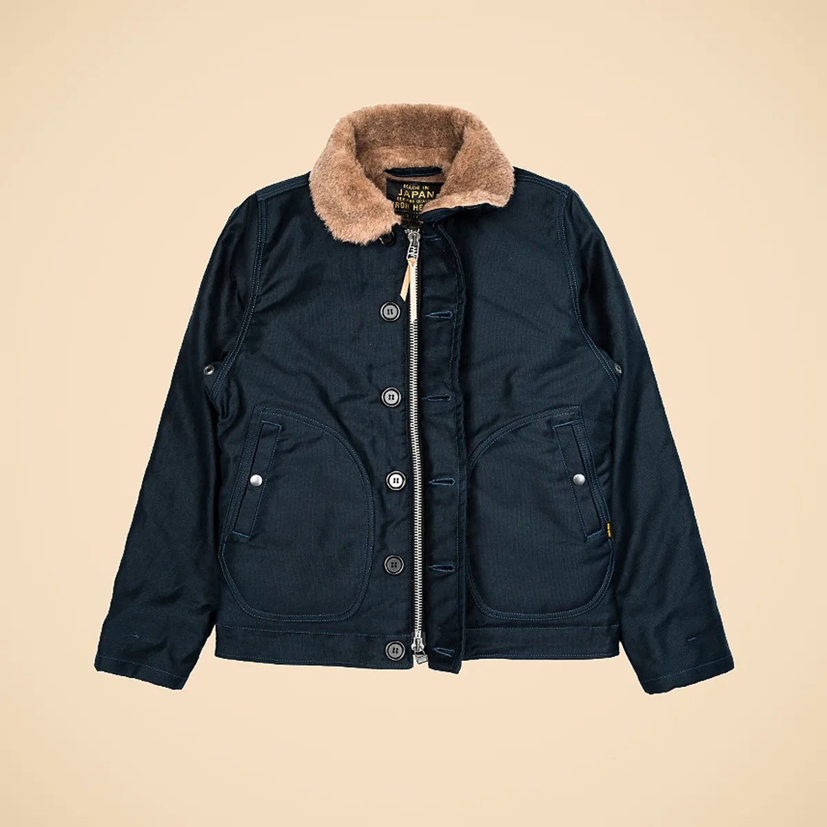 Navy blue jacket with tan faux fur collar, front zipper, button closure, and snap pockets on a beige background.