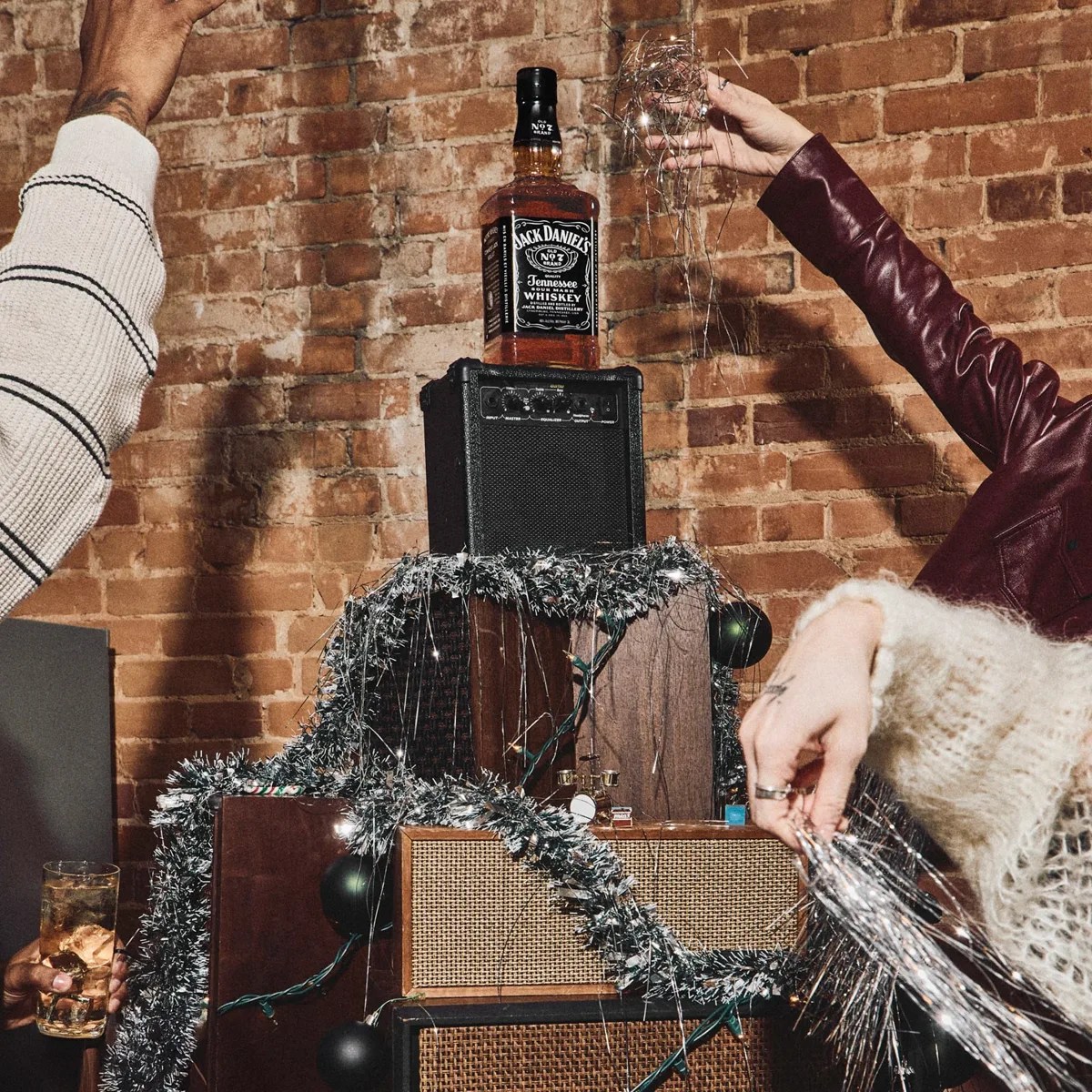Jack Daniel's whiskey bottle on a black amplifier decorated with silver tinsel against a brick wall.