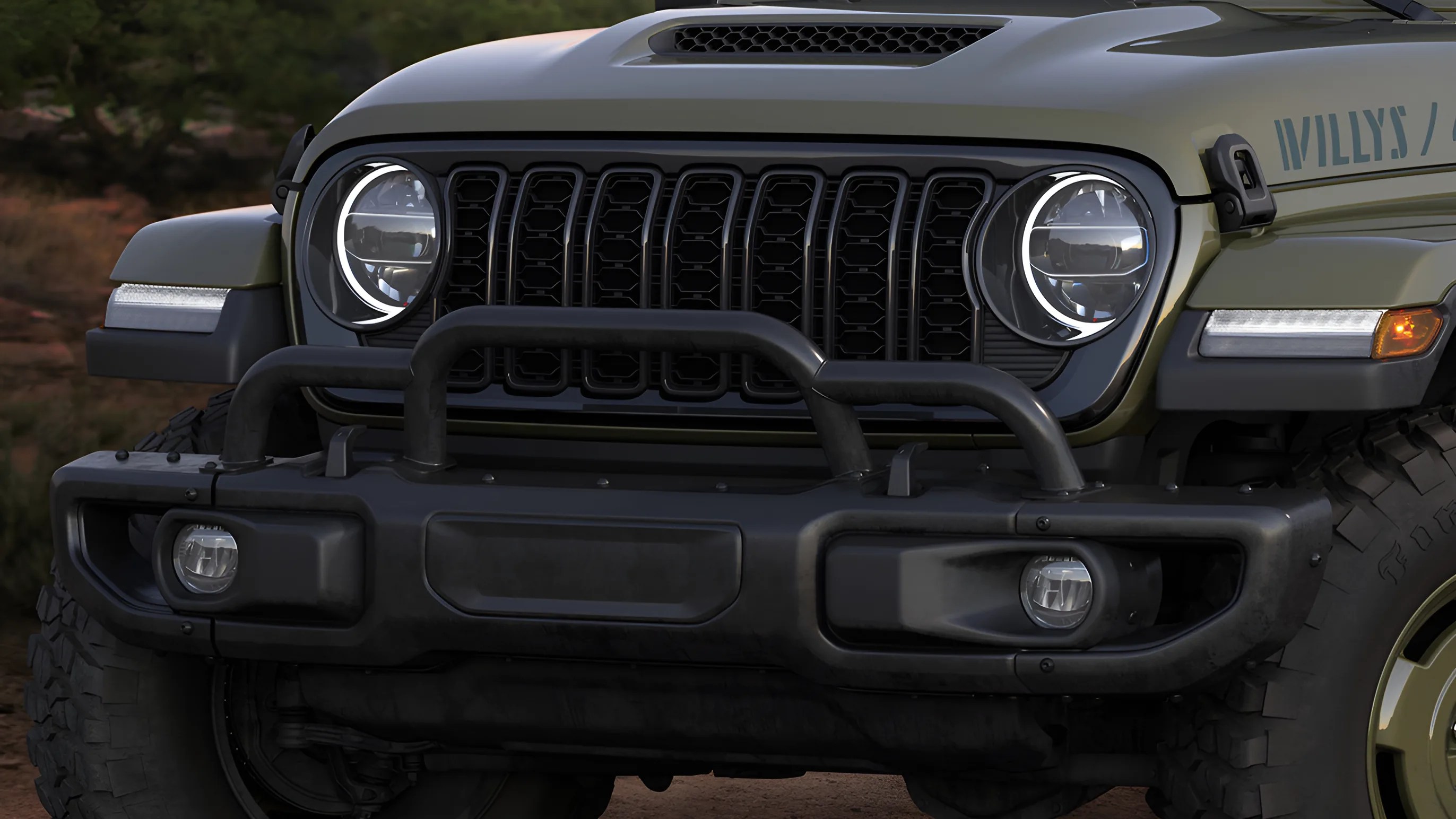 Front view of an olive green Jeep Willys with round LED headlights, black grille, and rugged bumper guard.