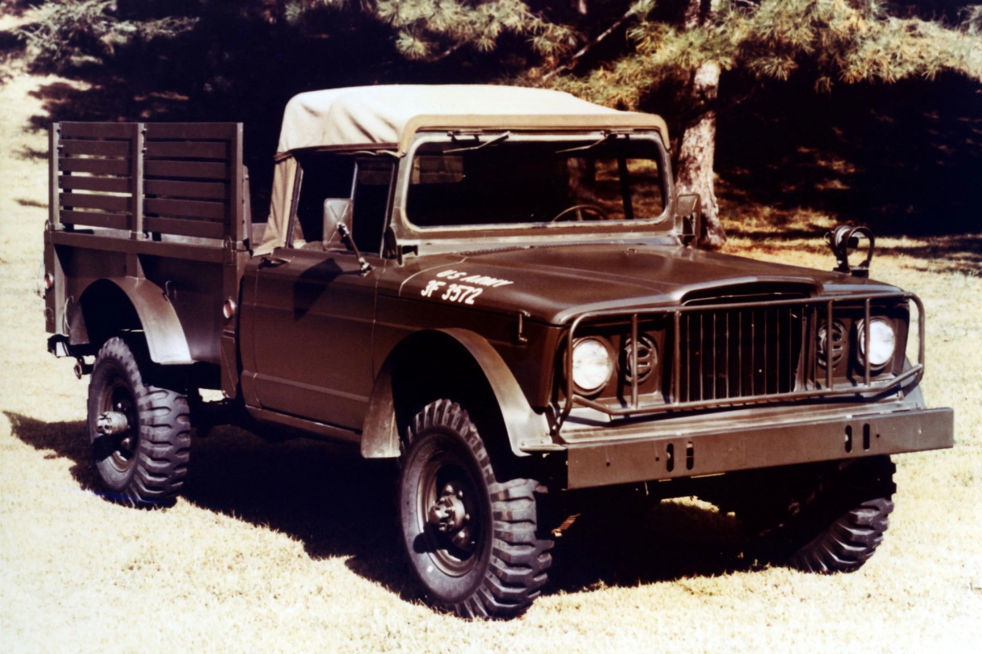 Olive drab military cargo truck with canvas roof and wooden side panels parked on grass.