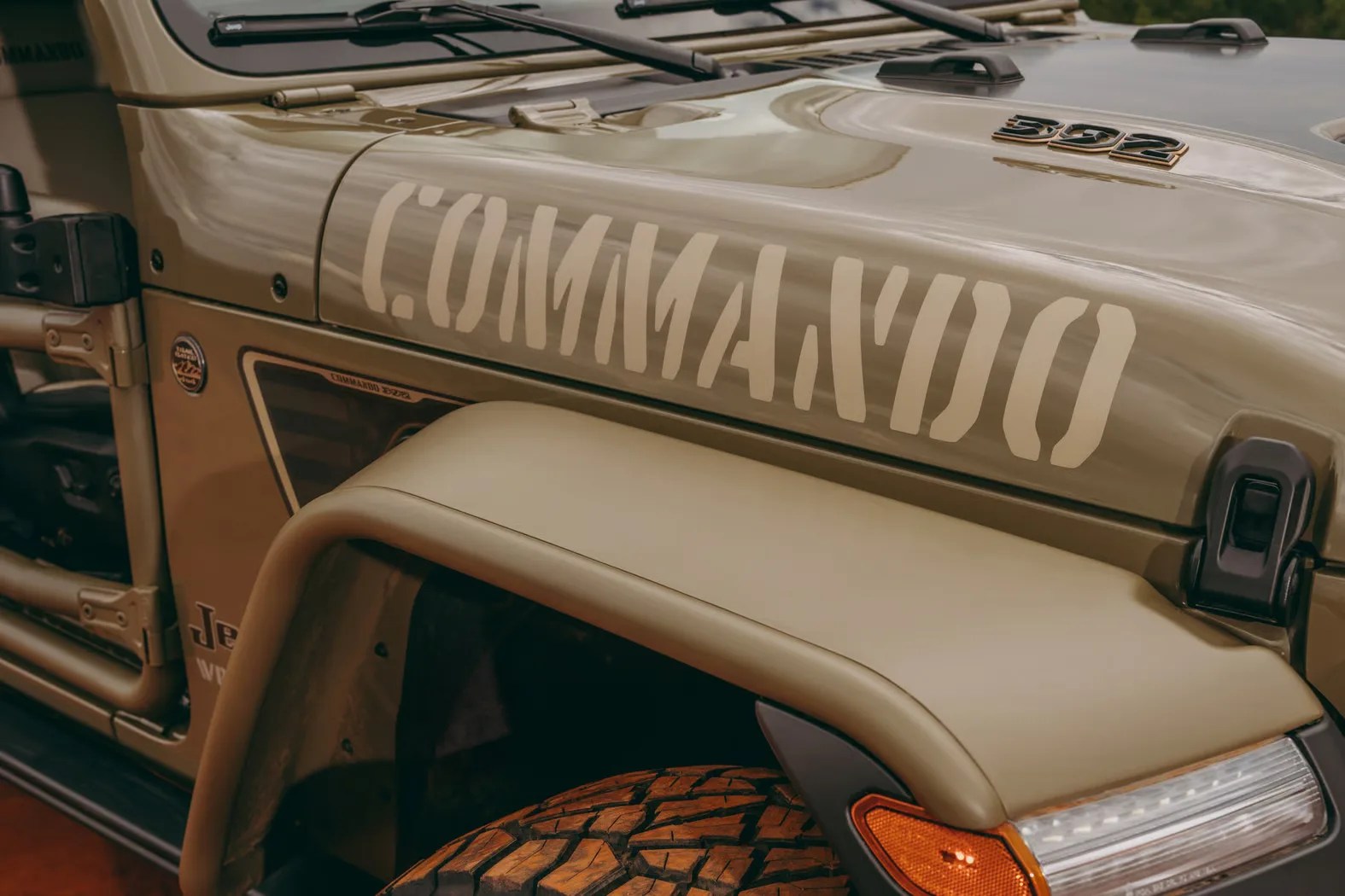 Close-up of a tan Jeep Wrangler with "COMMANDO" decal on the hood and "502" badge near the windshield.