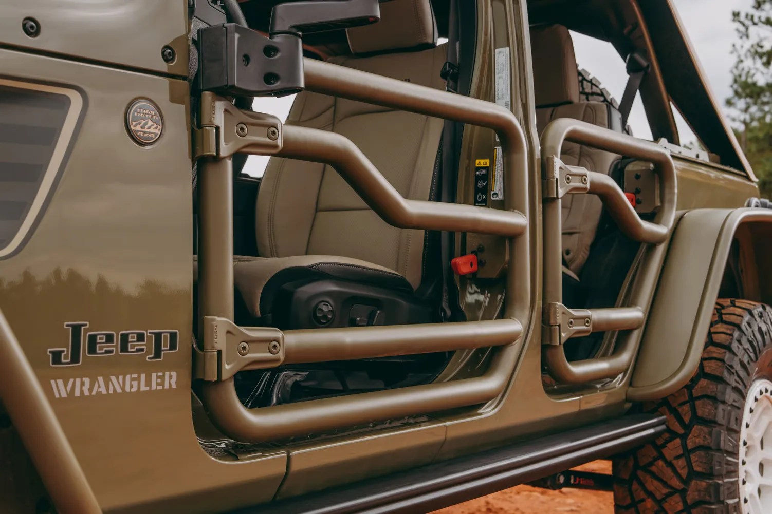 Open tubular metal doors on a tan Jeep Wrangler with beige seats and off-road tires.