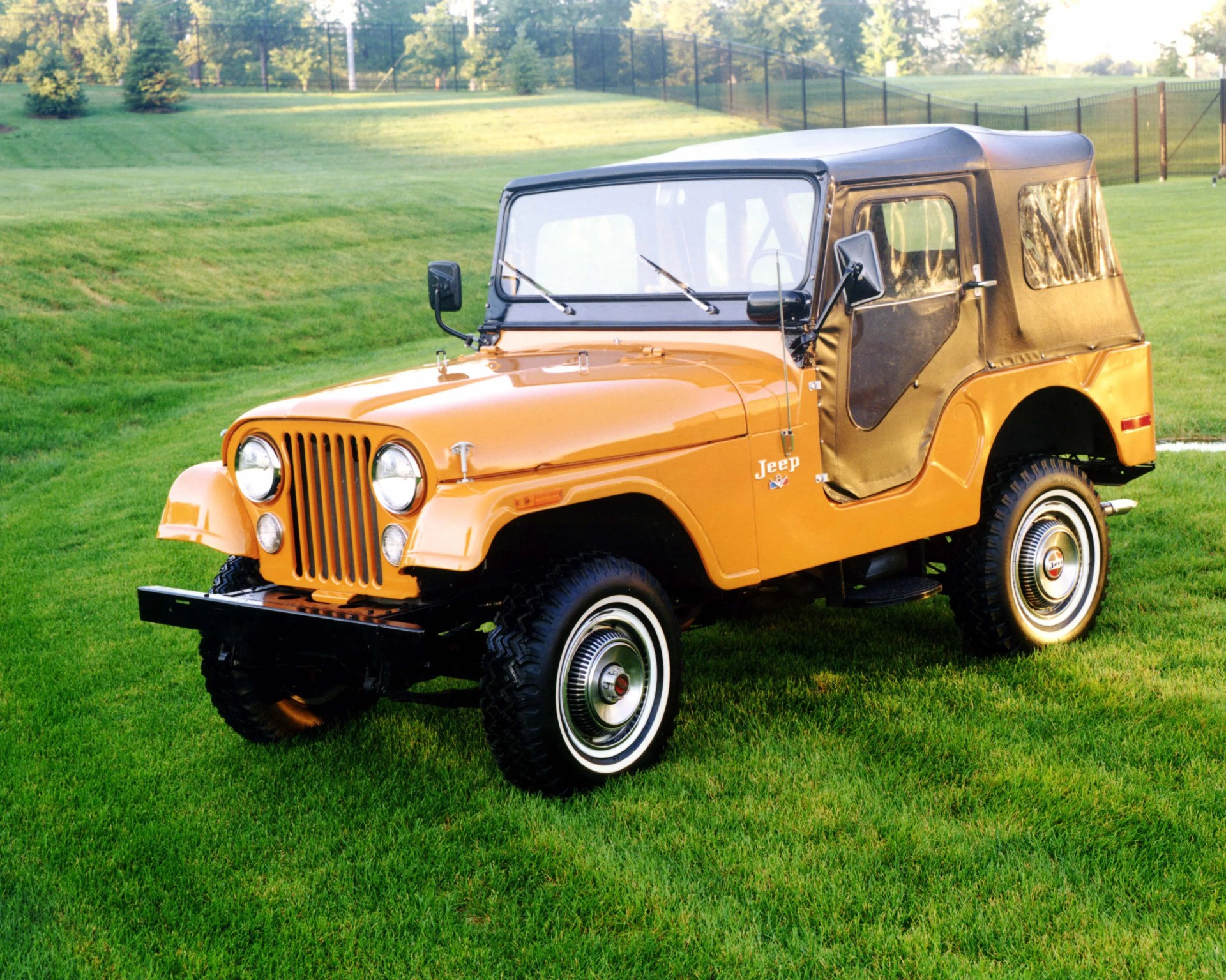 Orange vintage Jeep with black soft top parked on green grass.