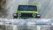 Bright green off-road vehicle driving through water with splashes in a forest setting.