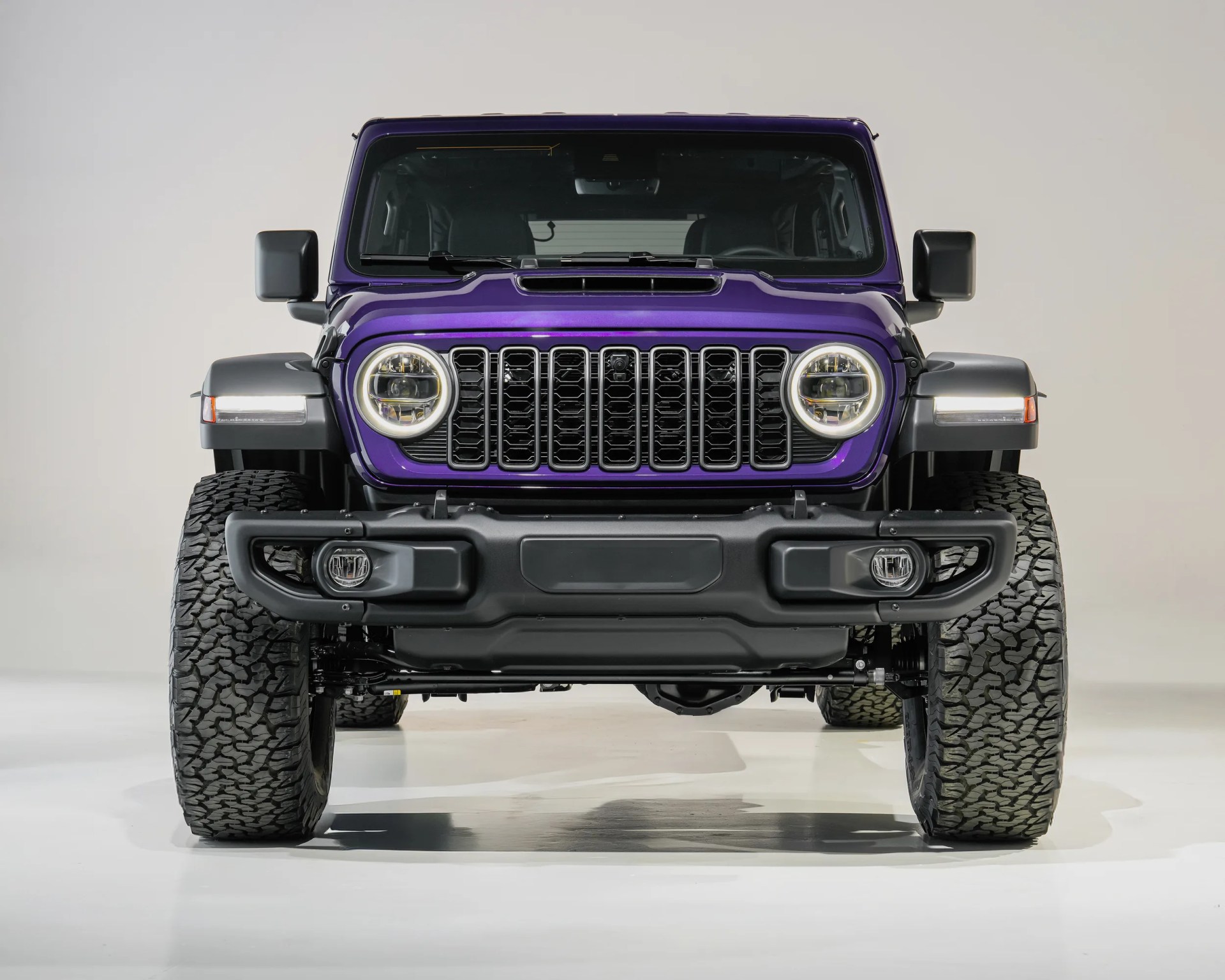 Front view of a purple off-road SUV with round LED headlights and large all-terrain tires on a white background.